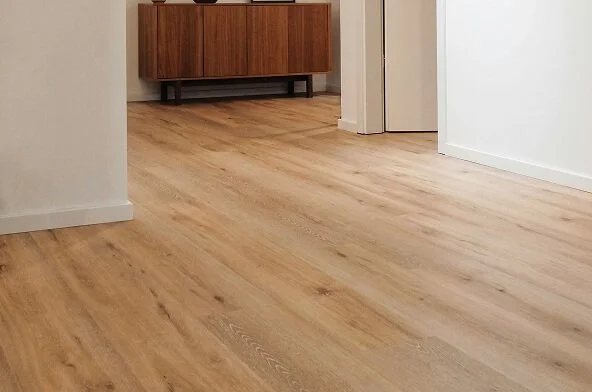 Empty room with light wood flooring, white walls, and a wooden sideboard against the back wall.