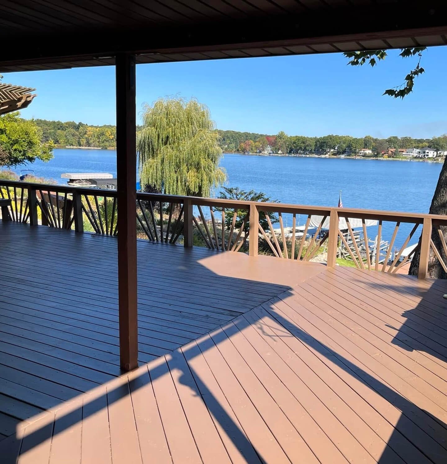 A wooden deck overlooking a lake with trees in the background, under a clear blue sky.