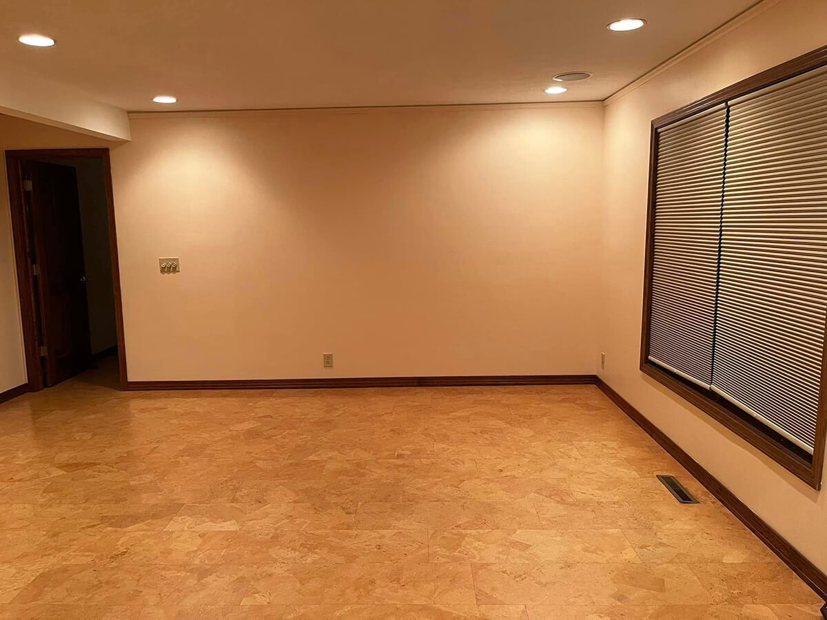 Empty room with beige walls, wooden flooring, window with closed blinds, and ceiling lights.