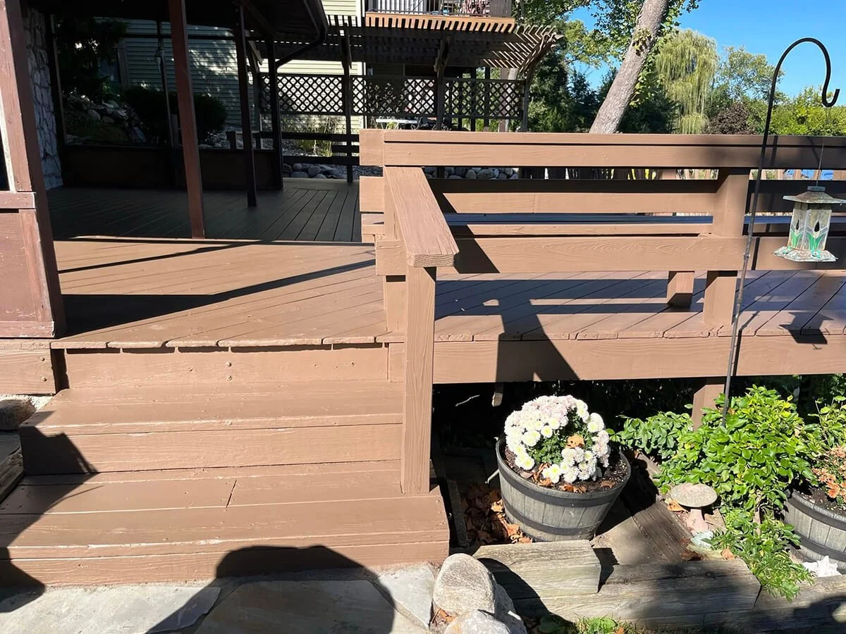 Backyard wooden deck with potted flowers, a garden bird feeder, and lush green trees in the background.