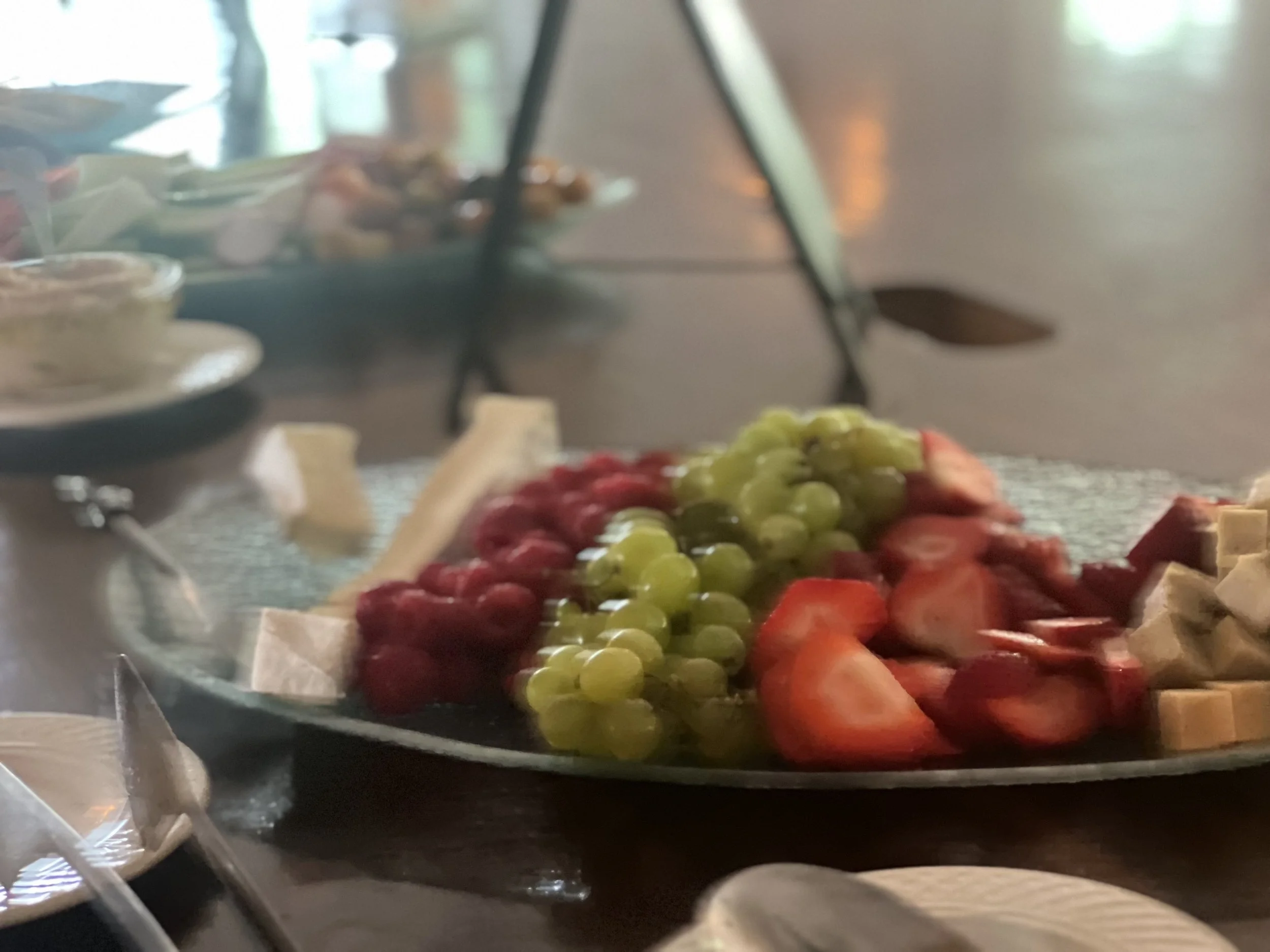 A close-up of a fruit platter with grapes, strawberries, and cubed cheese on a table.