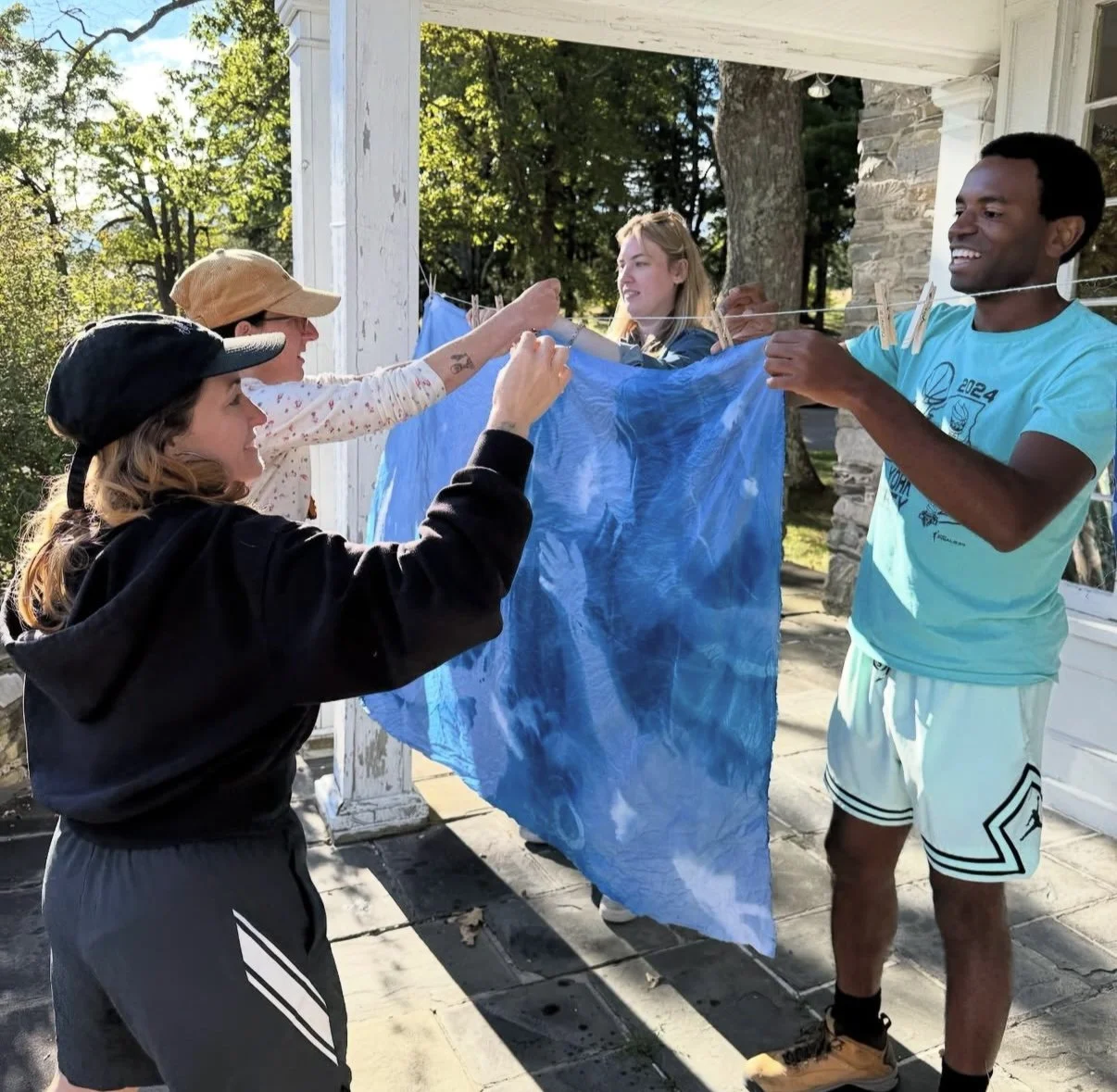 Four people hanging laundry to dry outdoors on a clothesline, smiling and enjoying a sunny day.