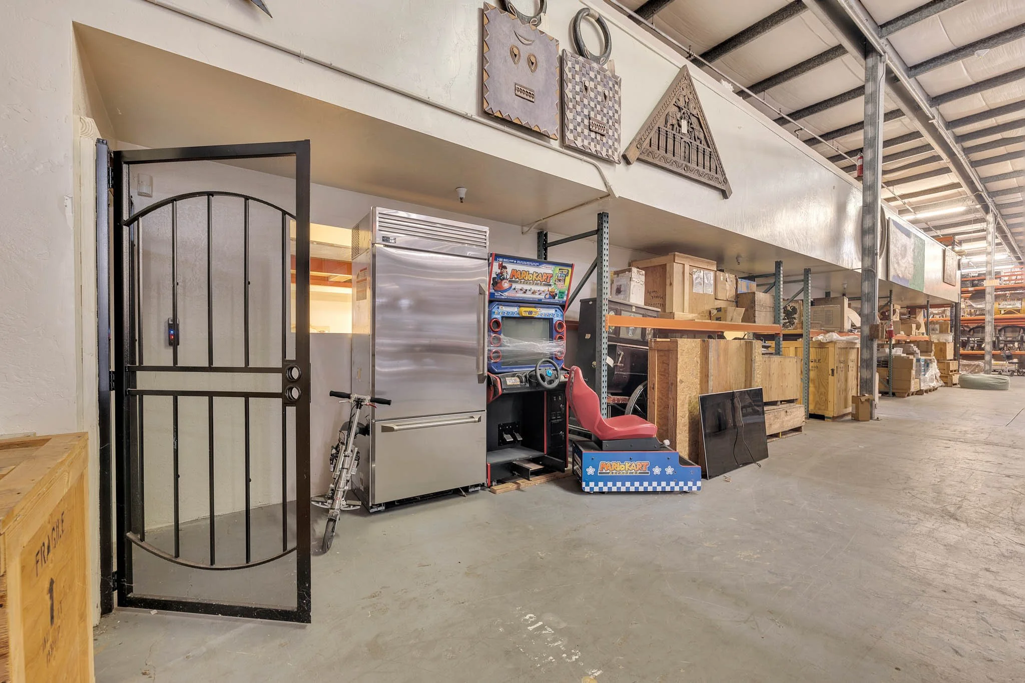 Warehouse with storage boxes, arcade game, motorcycle, and shelves with miscellaneous items.