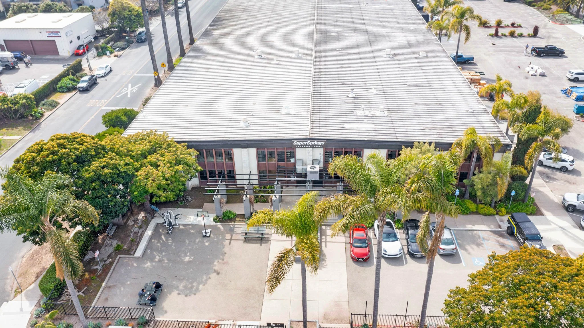 An aerial view of a building labeled 'SuperSprings International' surrounded by parking lots, trees, and palm trees, with several cars parked and a small outdoor basketball area.