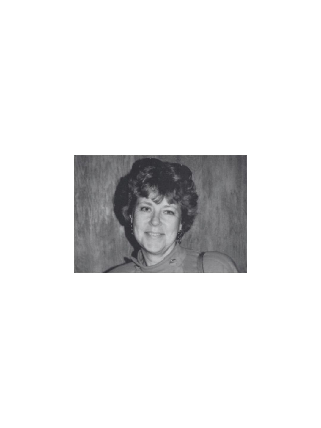 Black and white portrait of a woman with short curly hair, smiling, wearing earrings and a high-collared top.