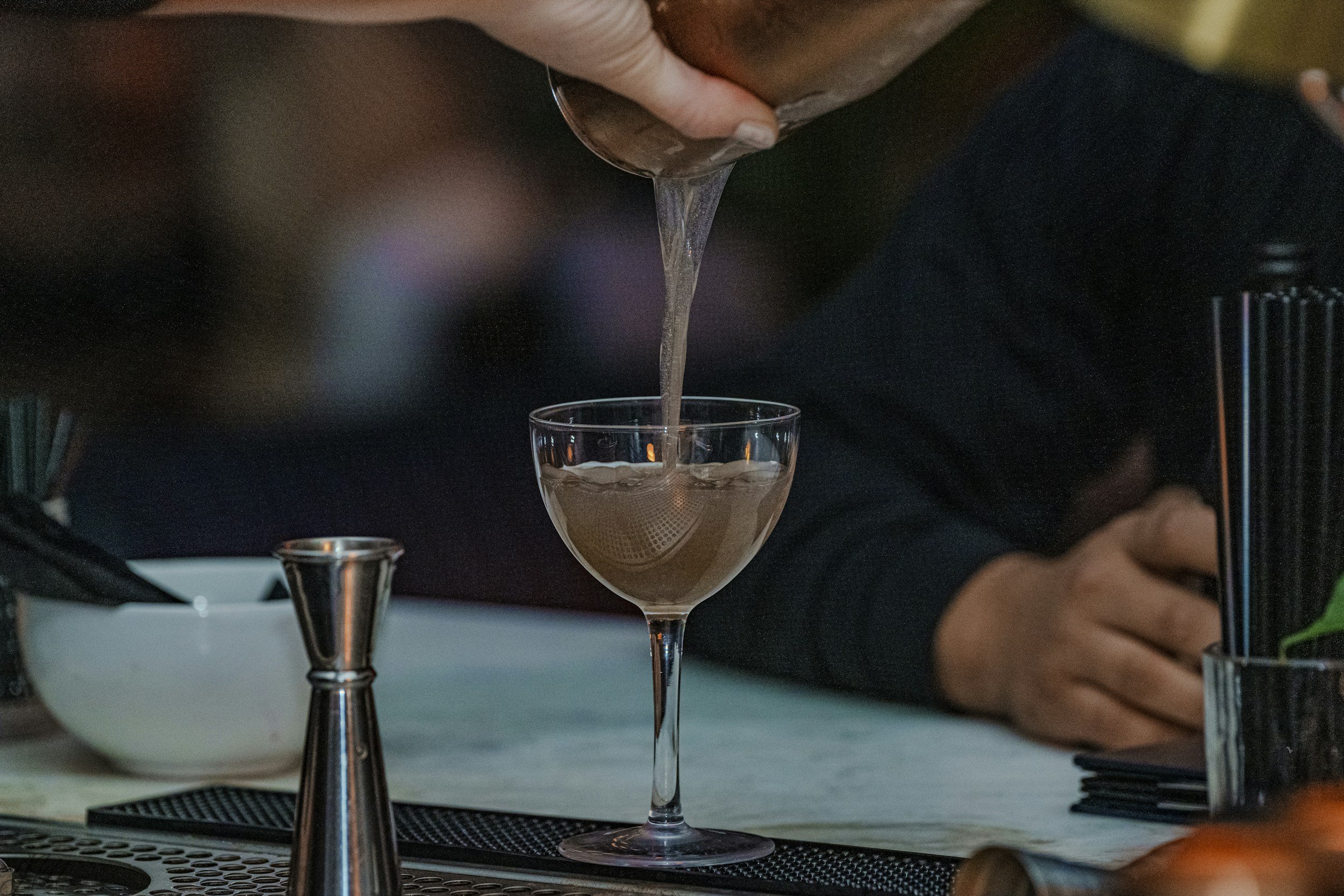 En person, der hælder en cocktail fra en shaker i et cocktailglas.
