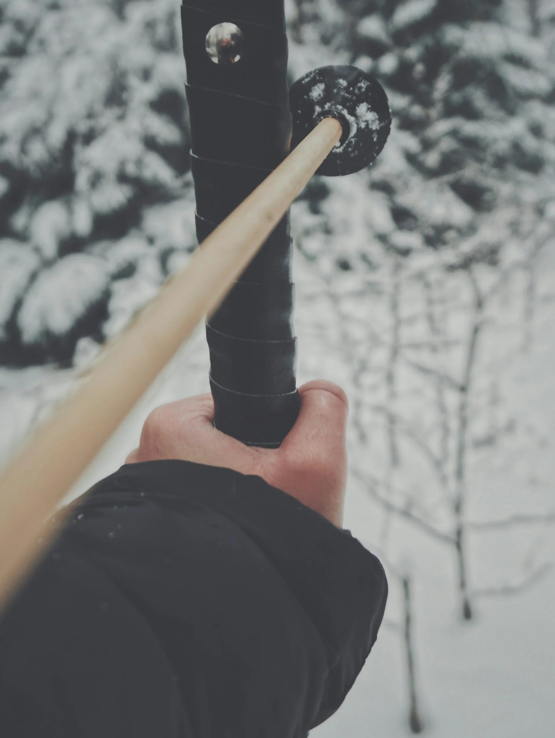 Close-up shot of a hand holding a hockey stick with a snow-covered background.