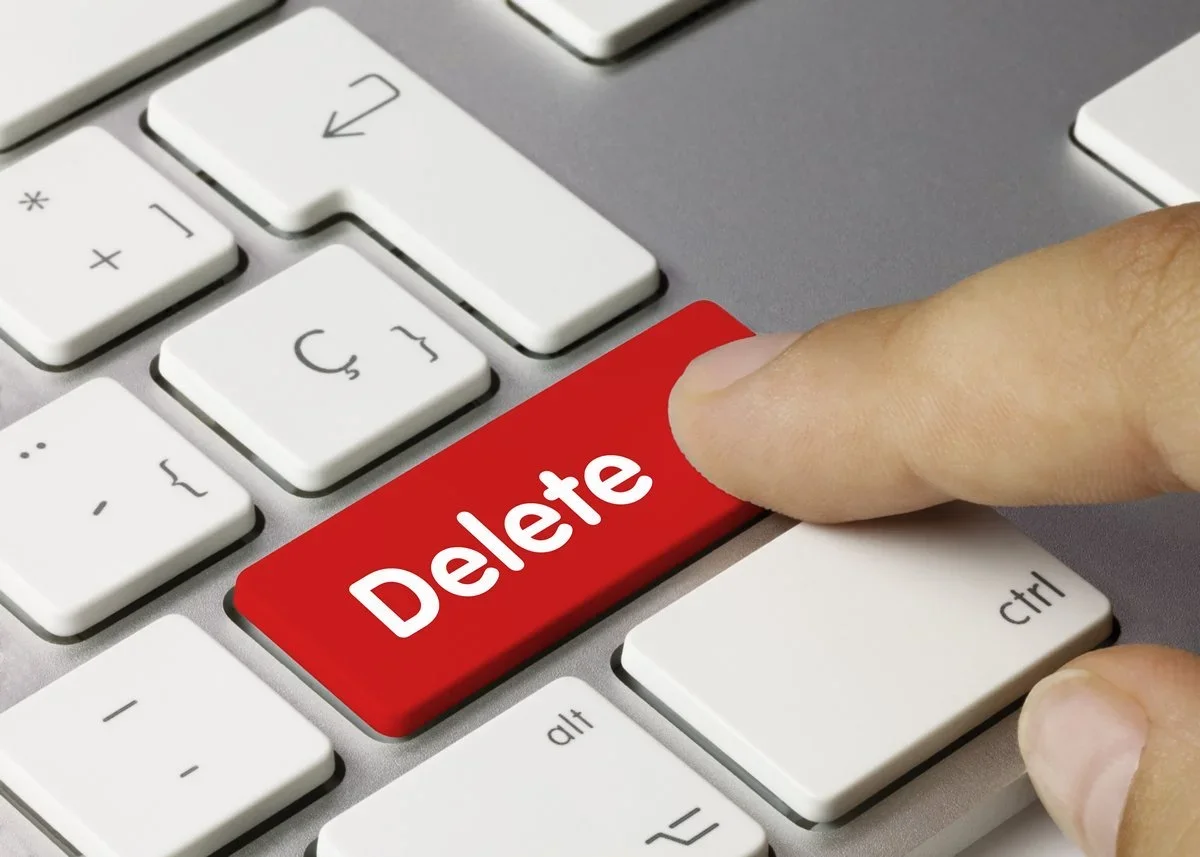 A hand pressing a large red “Delete” key on a keyboard, symbolizing digital decluttering and document cleanup.