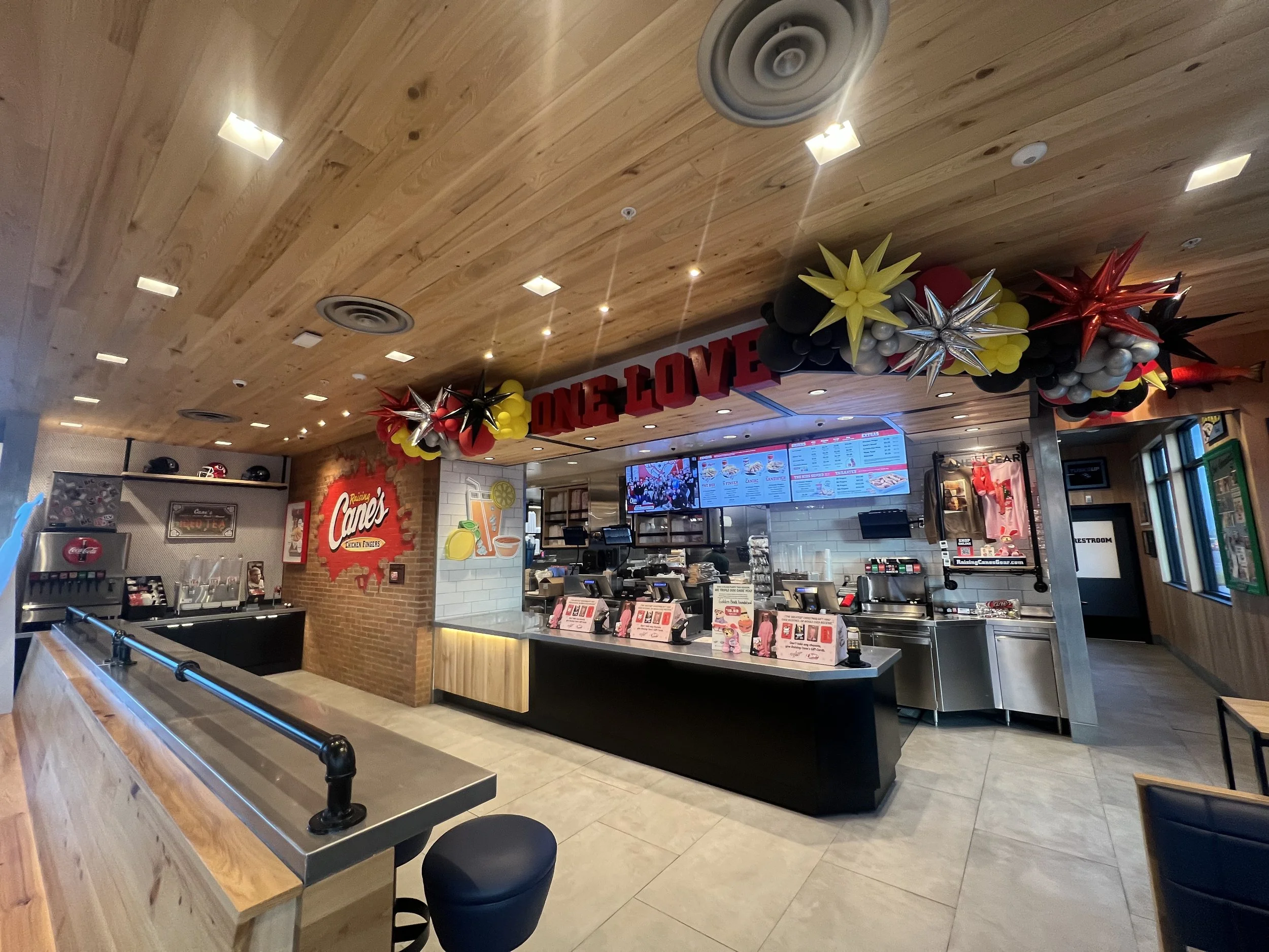 Interior of Raising Cane's fast food restaurant decorated with balloons and a 'ONE LOVE' banner for a celebration.