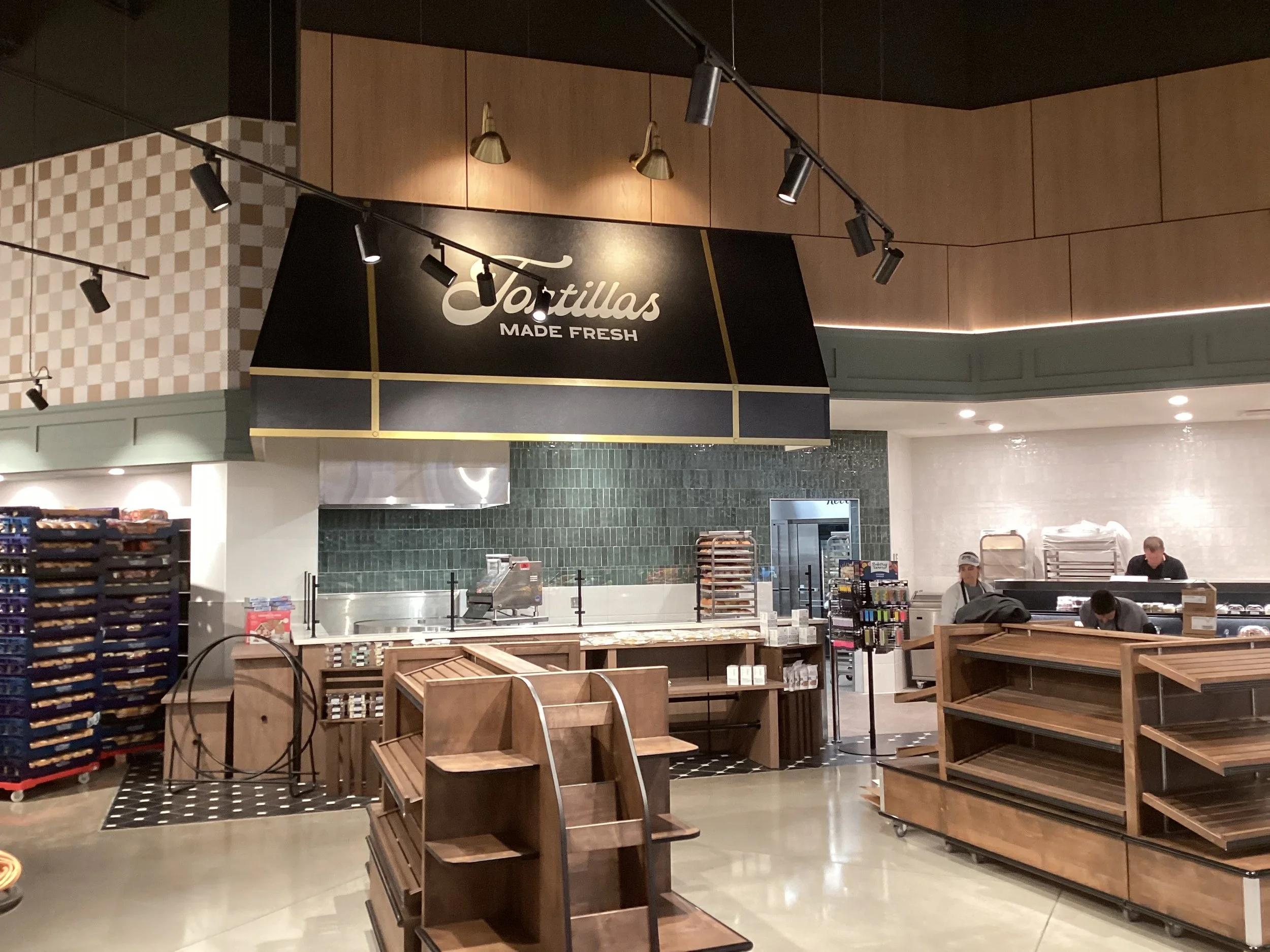 Interior of a grocery or retail store with empty wooden shelves and checkout counters, workers, and a sign that says "Tortillas Made Fresh."