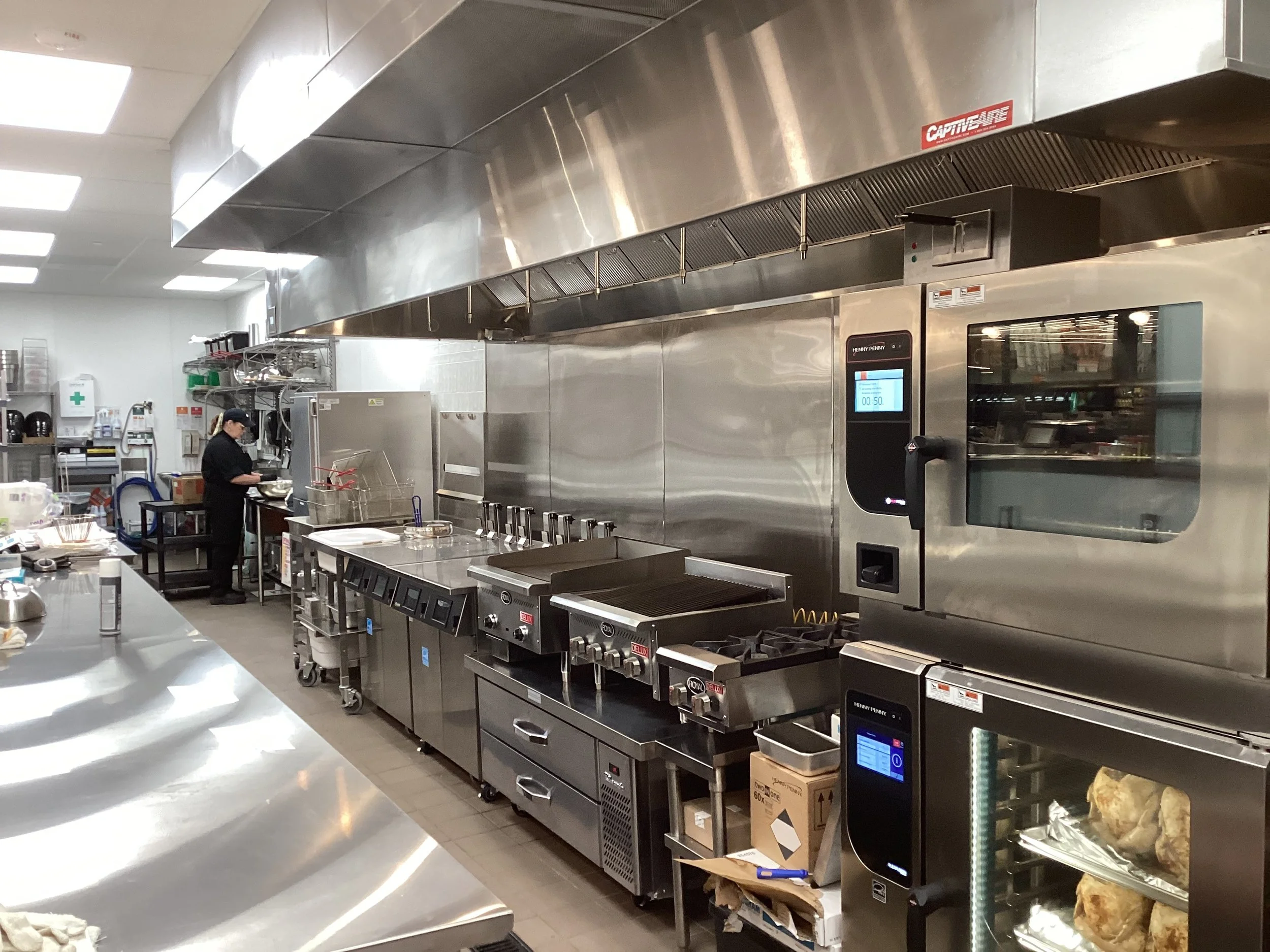 A professional commercial kitchen with stainless steel appliances and a person working at a station.