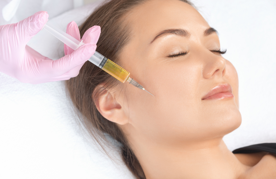 A woman with closed eyes receiving a cosmetic facial injection from a medical professional wearing pink gloves.