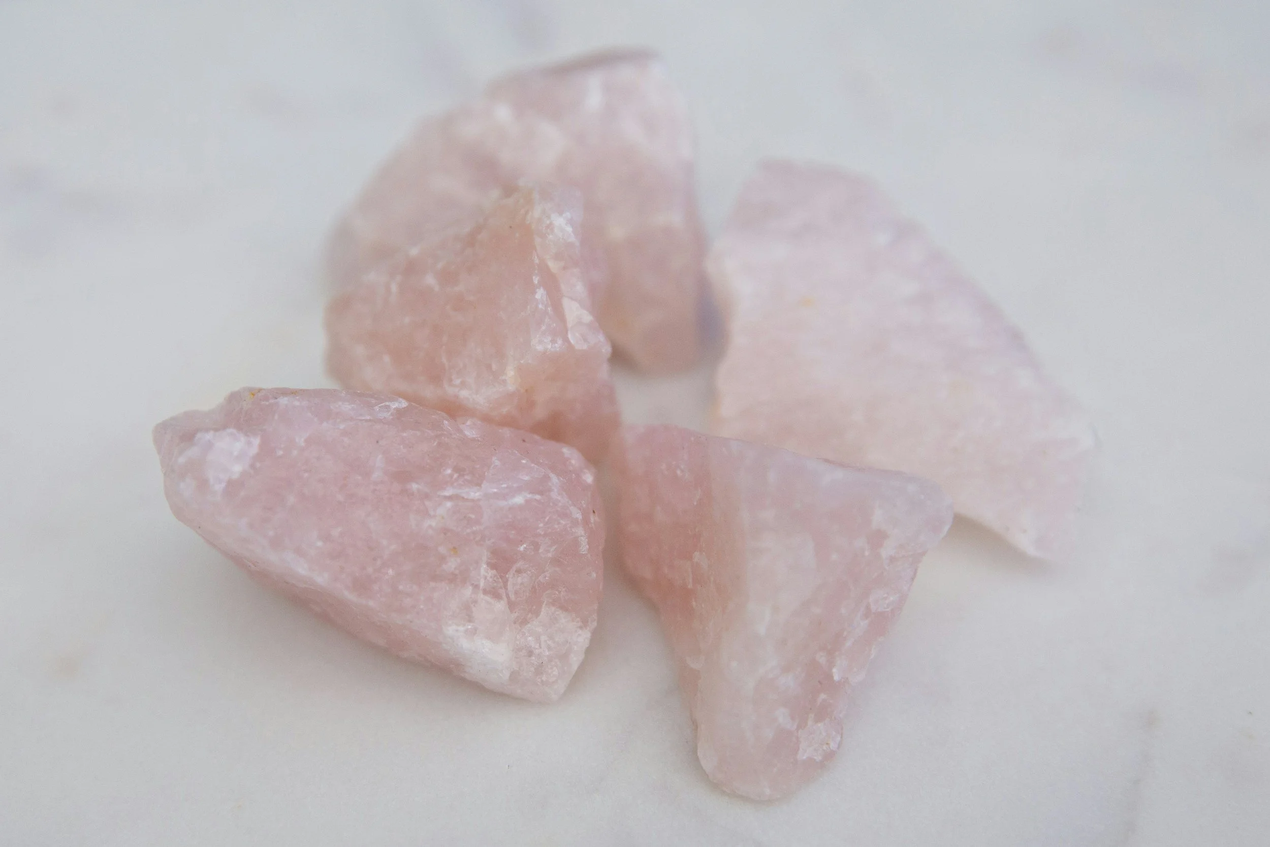 Five rough pink Himalayan salt crystals on a white surface.