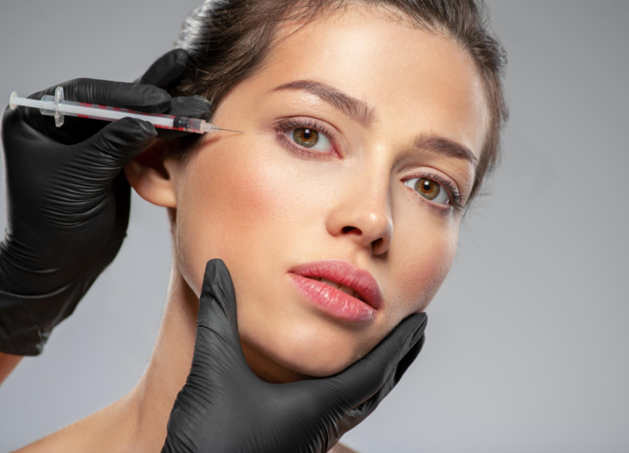A woman receiving a cosmetic injection near her eye from a healthcare professional wearing black gloves.