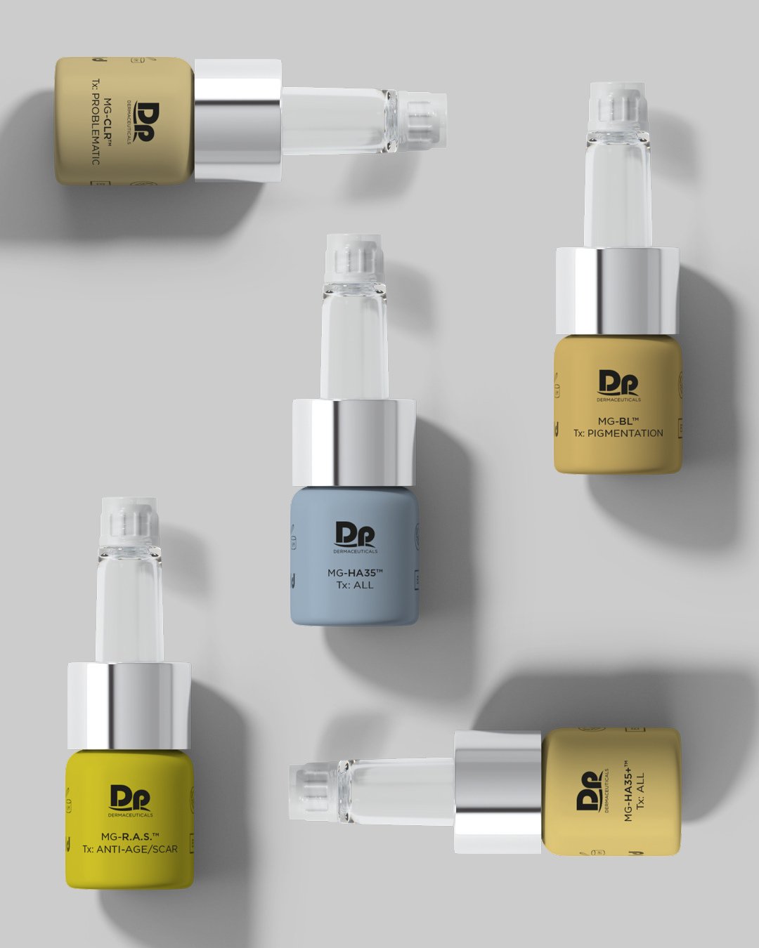 Collection of six small bottles of dermaceutical skincare serums arranged on a light gray surface, with six clear dropper caps, some with colorful labels in yellow, blue, and gray.