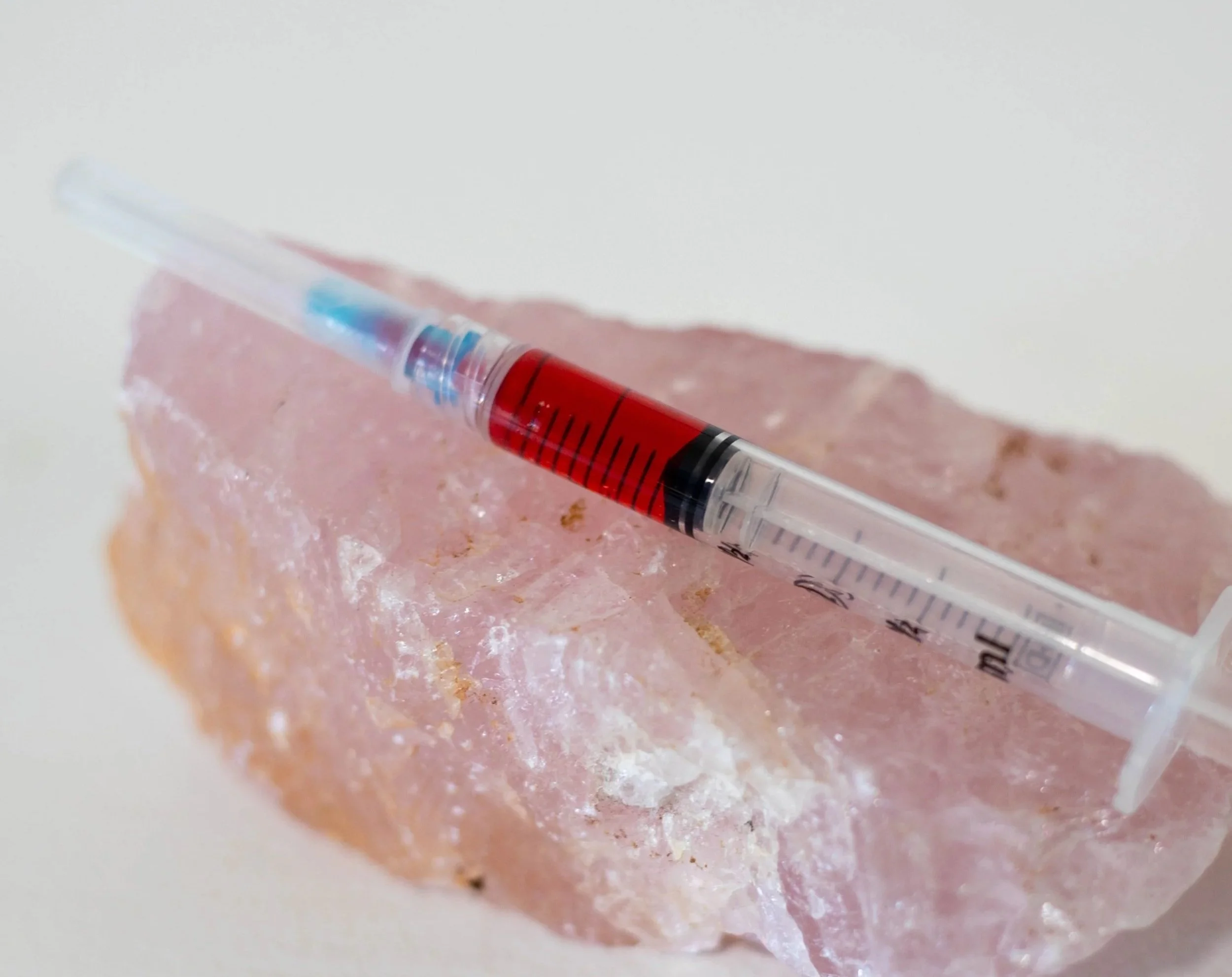 A syringe filled with red liquid resting on a pink rock.