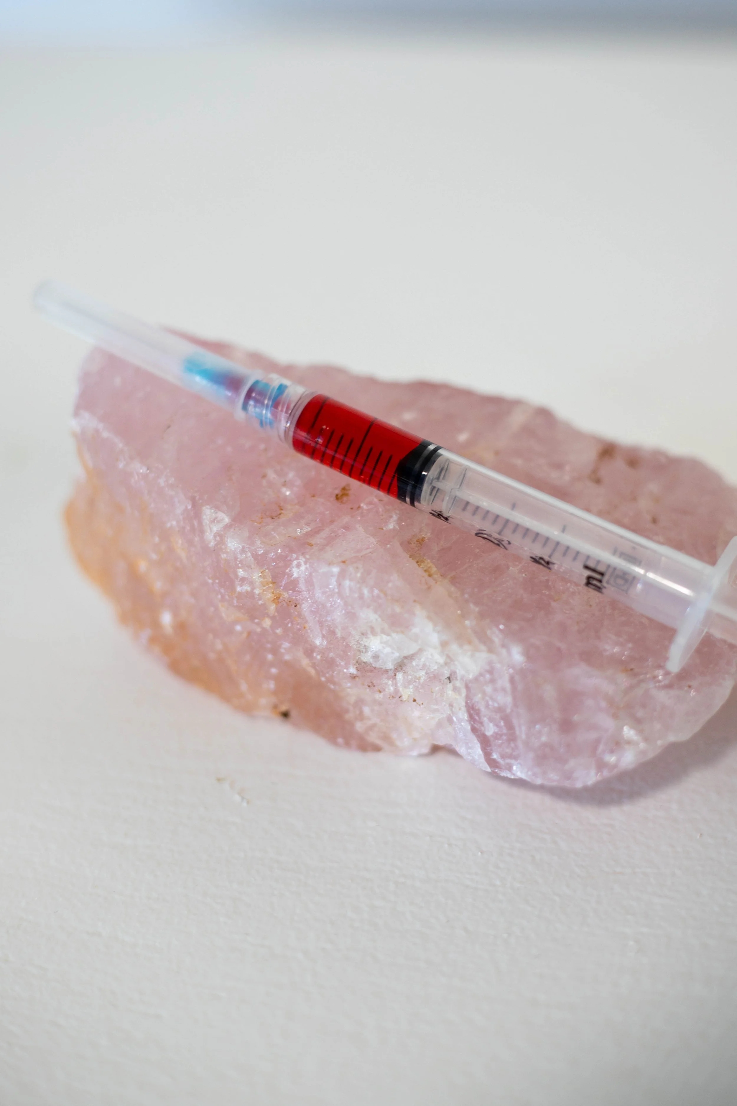A syringe filled with red liquid resting on a pink mineral or salt rock on a white surface.