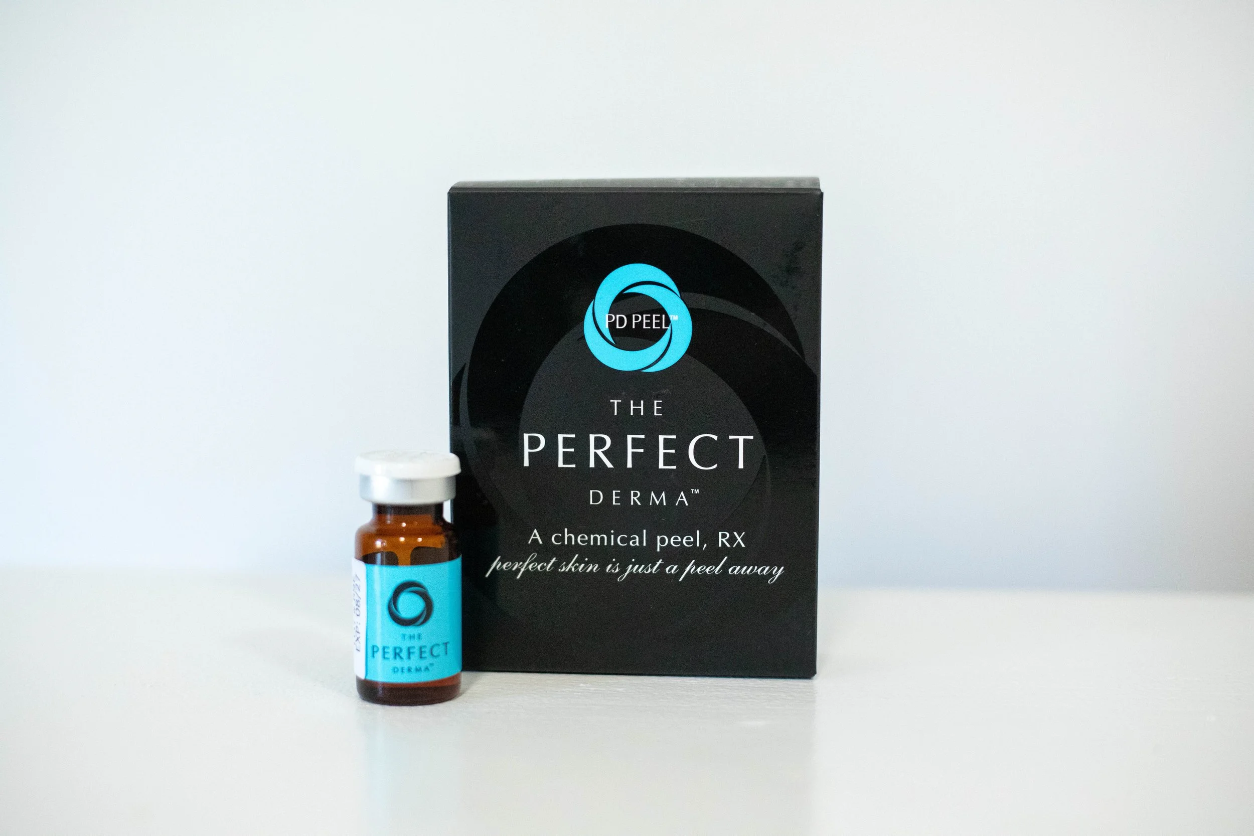 A box and a small bottle of THE PERFECT DERMA chemical peel product on a white surface against a white background.