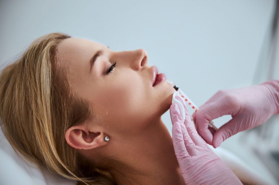 A woman lying down with her eyes closed, receiving a medical test on her neck from a person wearing pink gloves.