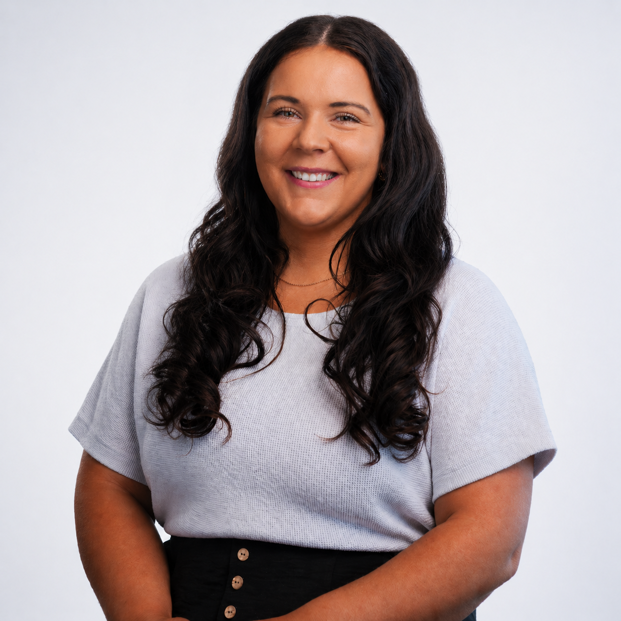 Meet our operations director, Whitney Rales. Portrait of a woman with long dark hair, smiling, wearing a black top and a cream-colored jacket, standing outdoors with a blurred background.