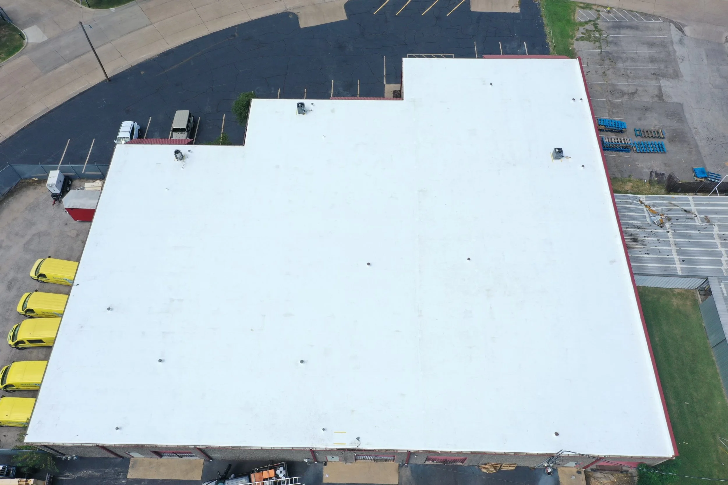 A person on a commercial roof on a white flat rooftop holding an orange bag, with a clear blue sky in the background.