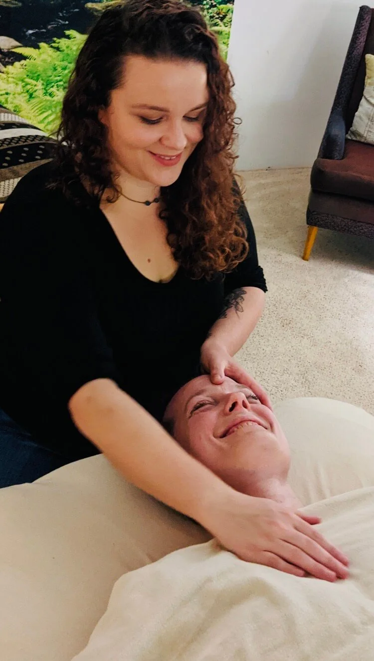 A woman with curly hair giving a massage to a man lying on a bed, smiling and relaxing.