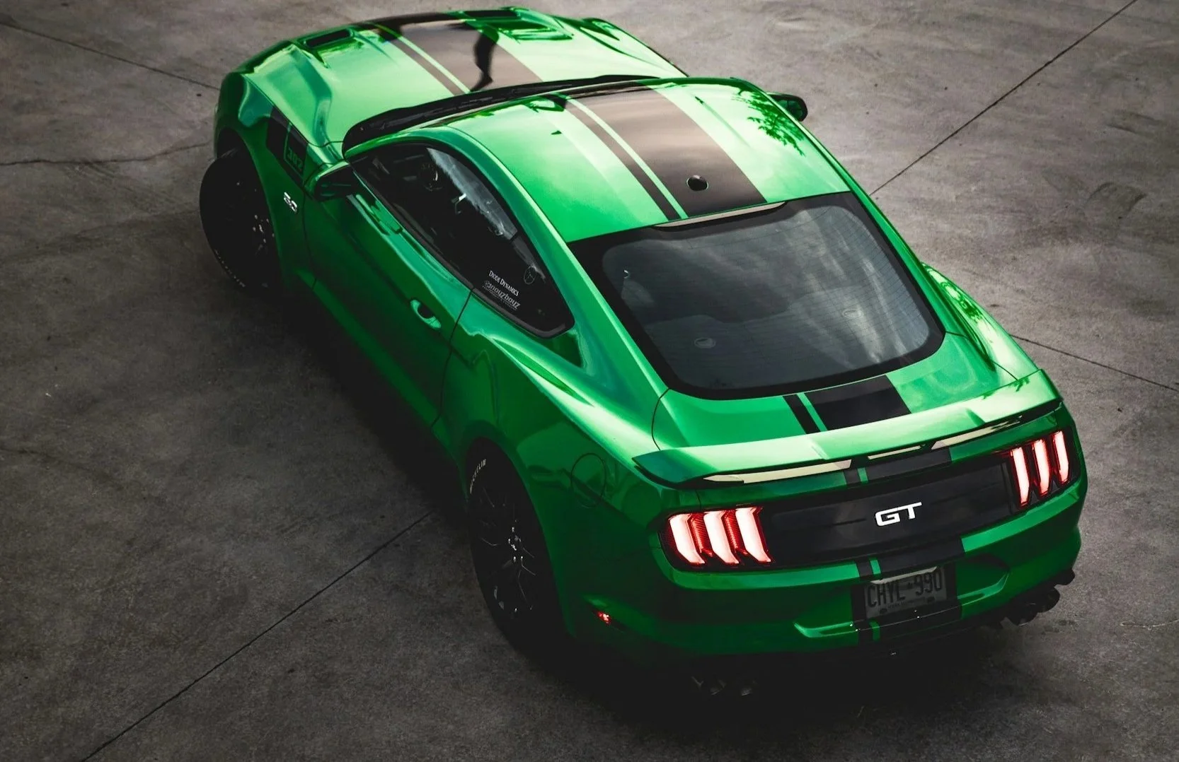 Green Ford Mustang GT with black racing stripes, viewed from above on a concrete surface.
