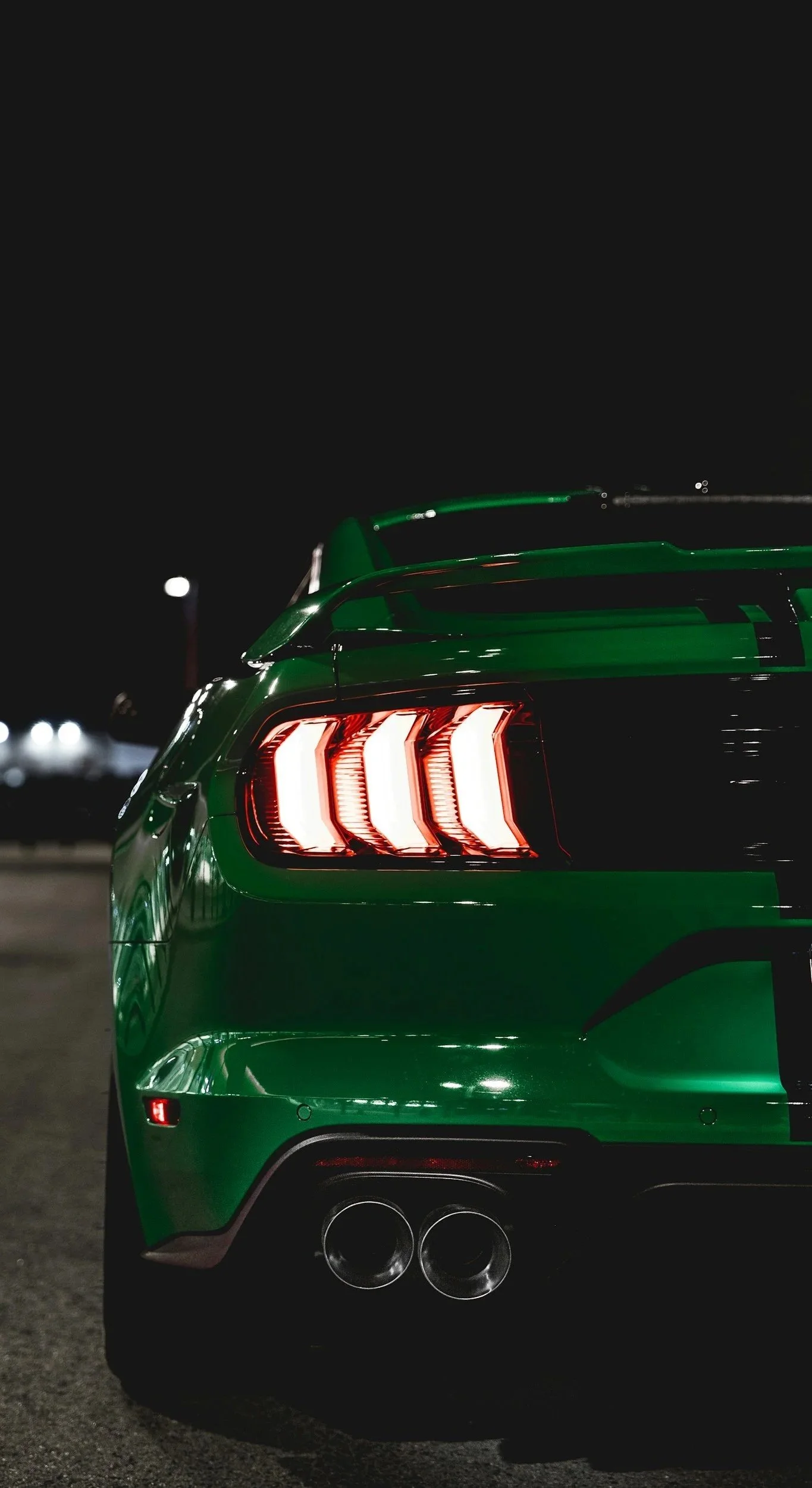 A green sports car with illuminated taillights and dual exhaust pipes parked at night.