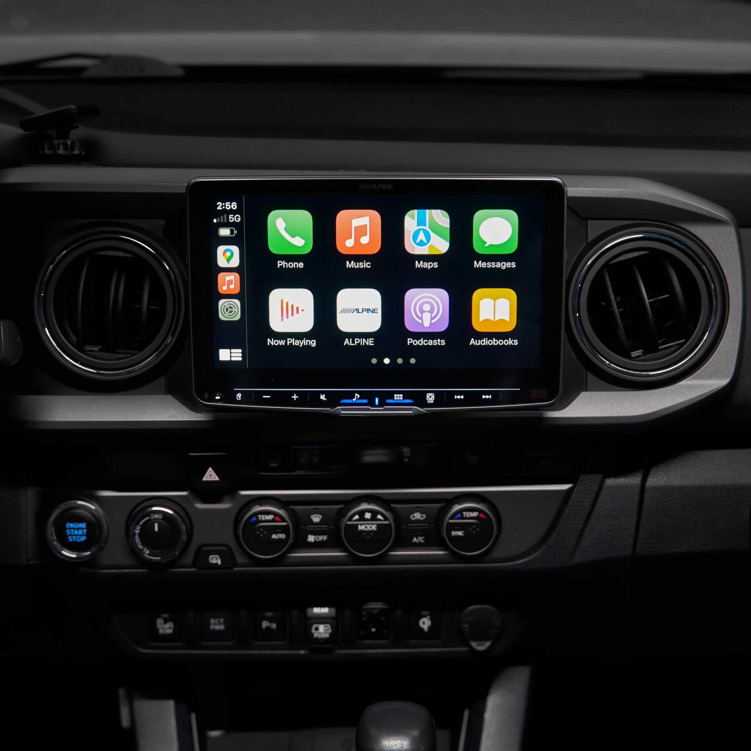 Car dashboard with a central touchscreen displaying Apple CarPlay menu, surrounded by air vents and climate control buttons.