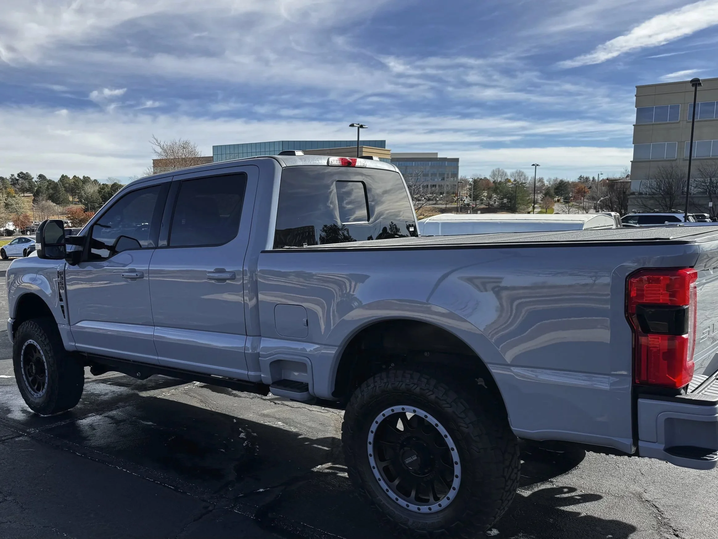 A silver pickup truck parked on an outdoor parking lot, with a blue sky and modern buildings in the background.