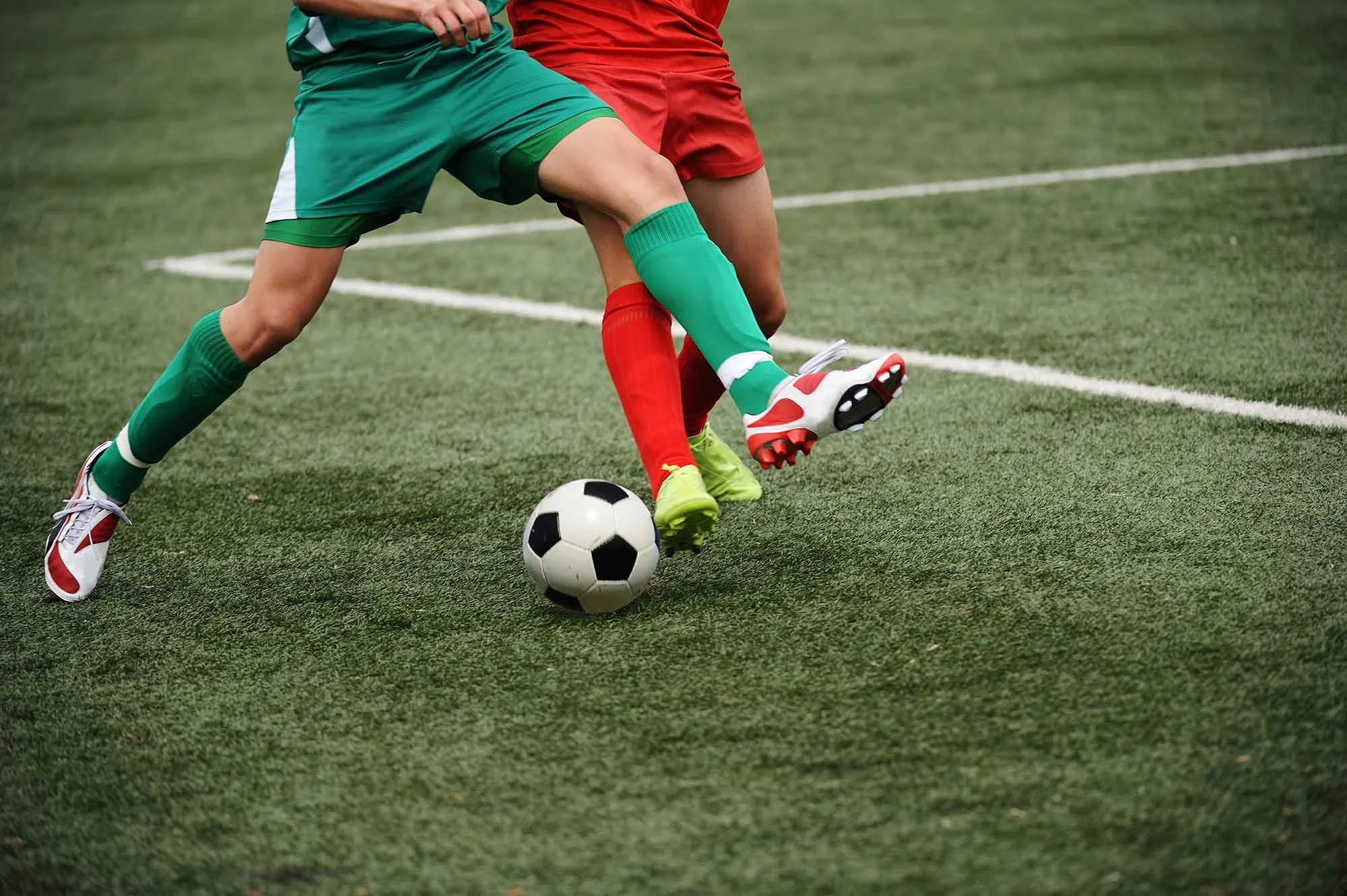 soccer-football-players-kicking-ball-turf.jpg