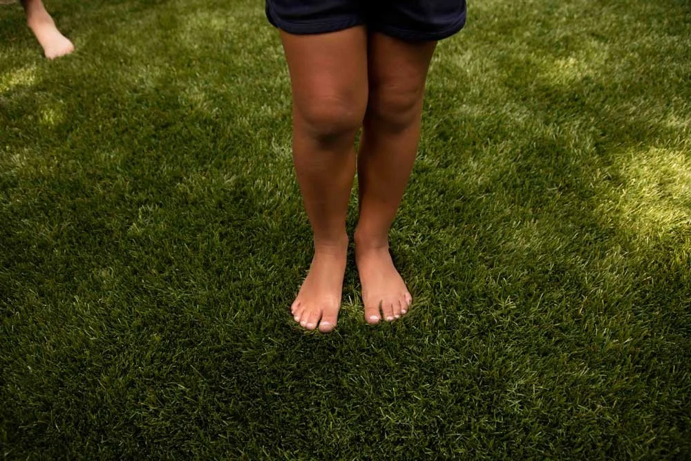Person standing barefoot on an artificial grass lawn, wearing dark shorts.