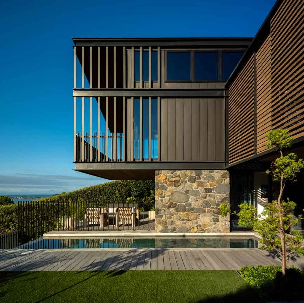 Aerial view of modern suburban homes beside a pond, landscaped with green lawns and surrounded by open space under a clear sky.