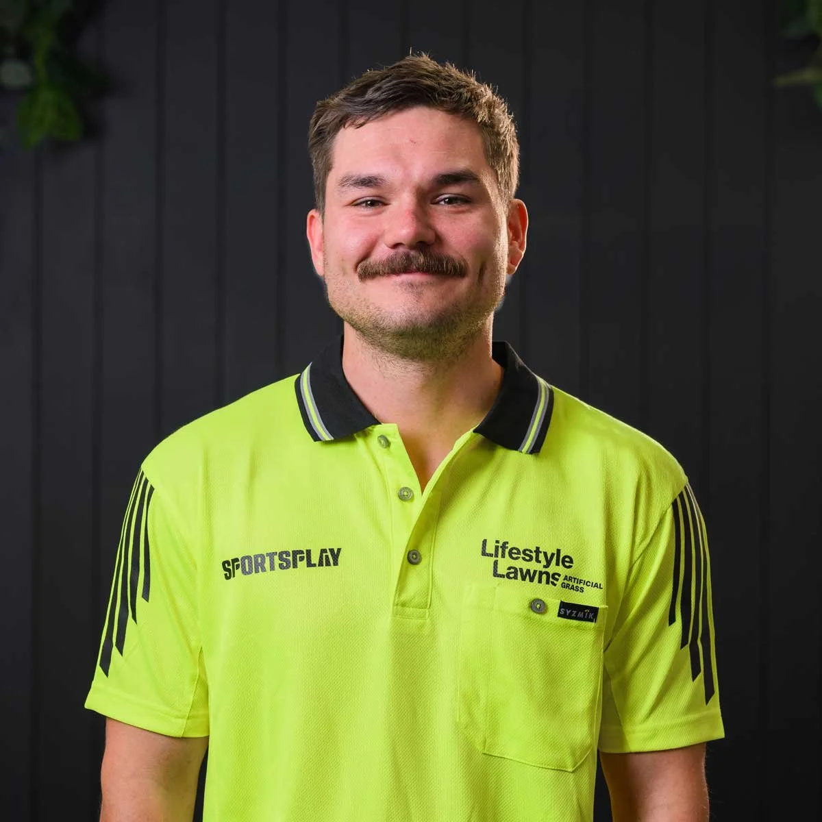 Joe from Lifestyle Lawns, smiling, standing in front of a dark wooden background.