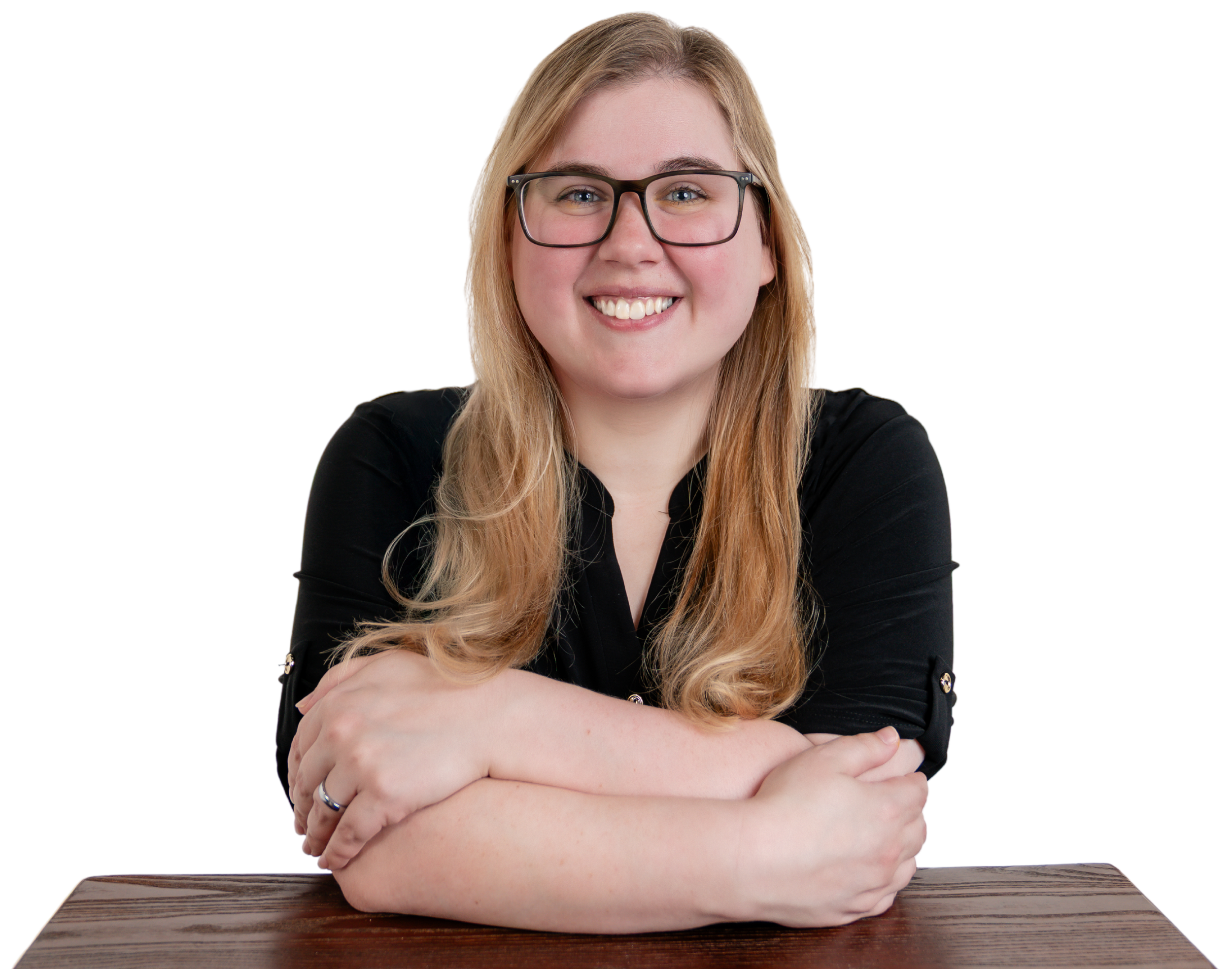 Smiling woman with glasses in a black shirt sitting at a wooden table with arms crossed