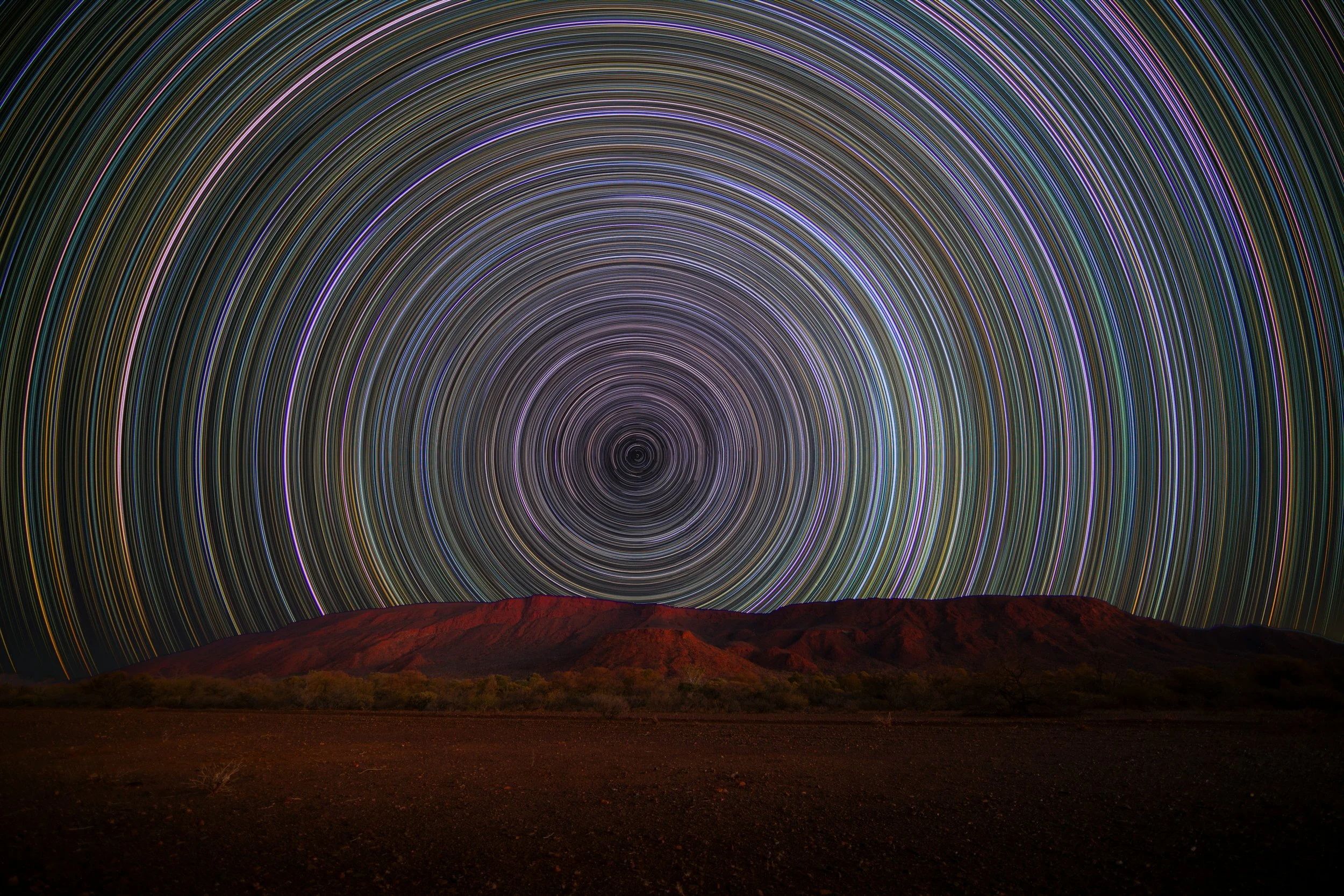 Night sky with time lapsed stars over a desert landscape resulting in concentric rings of light. Photo by Brian McMahon via Unsplash