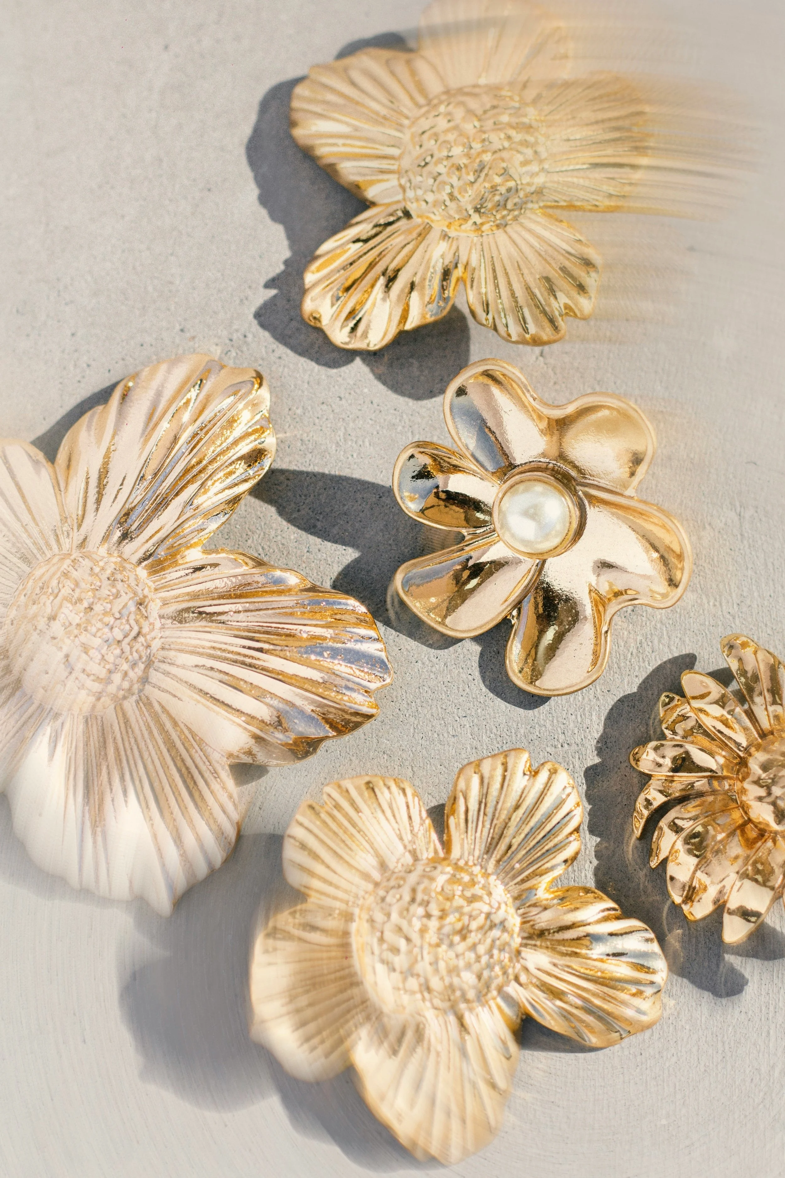 A close-up of four, gold flower brooches on light gray concrete. Photo by Ruan Richard Rodrigues via Unsplash