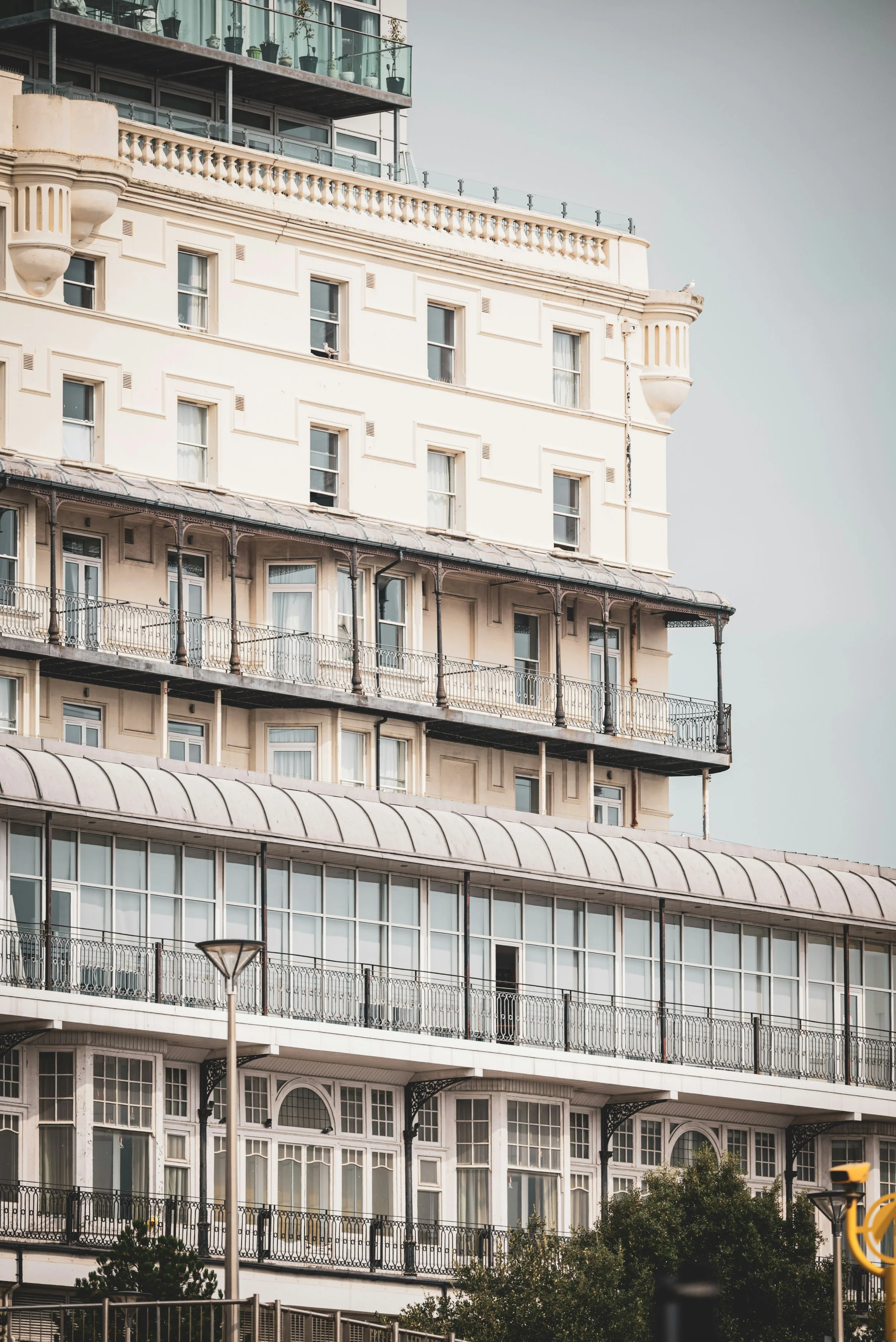 A multi-story building with intricate architectural details, including balconies with ornate railings, multiple windows, and a mix of modern and classical design elements. The sky is overcast, and there are some trees and street lights in the foreground.