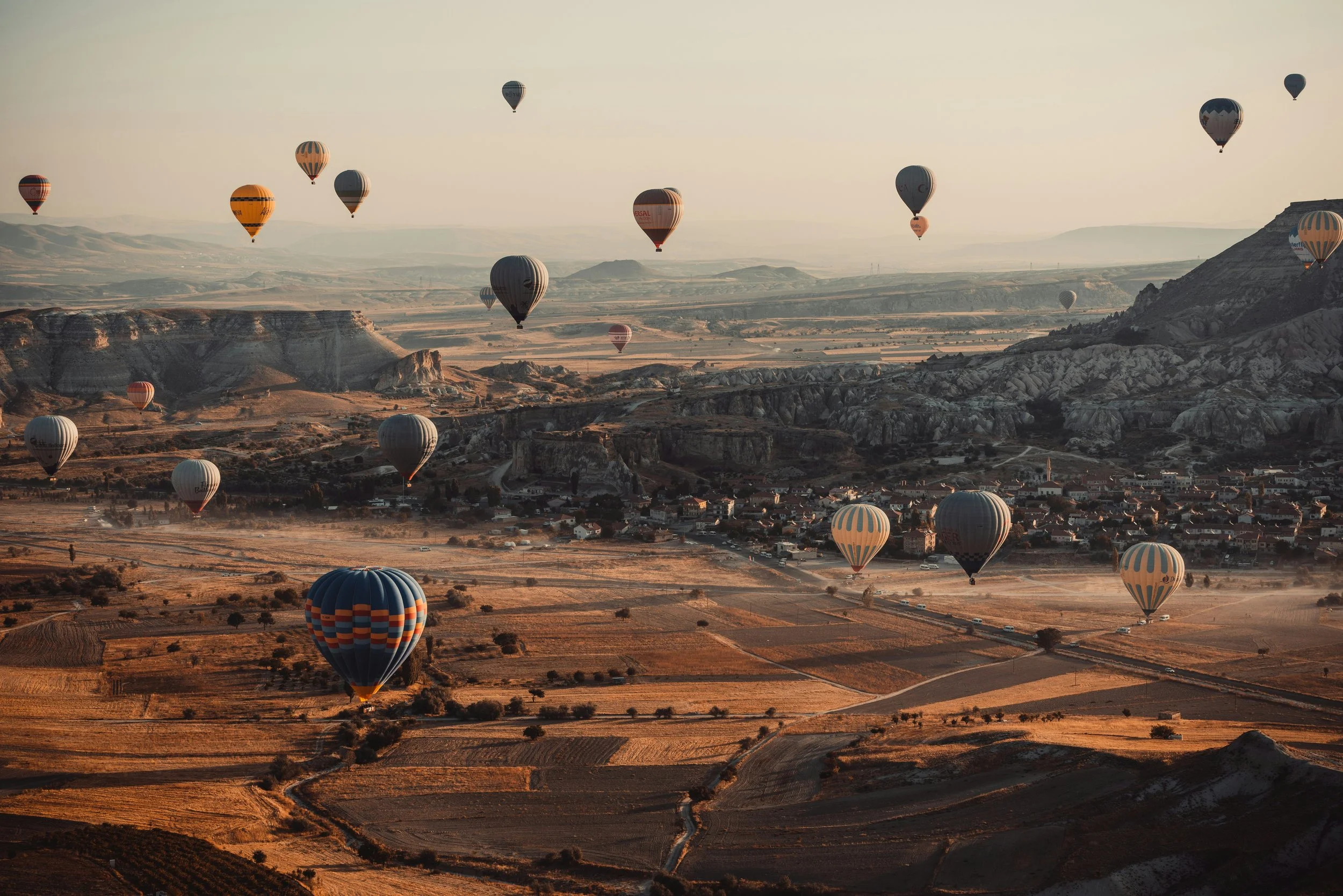 Multiple hot air balloons floating over a scenic, mountainous landscape at sunrise or sunset.