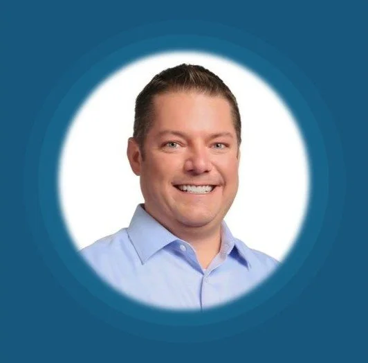 Trent Fouts's Headshot of a smiling man wearing a light blue collared shirt against a blue and white circular background.