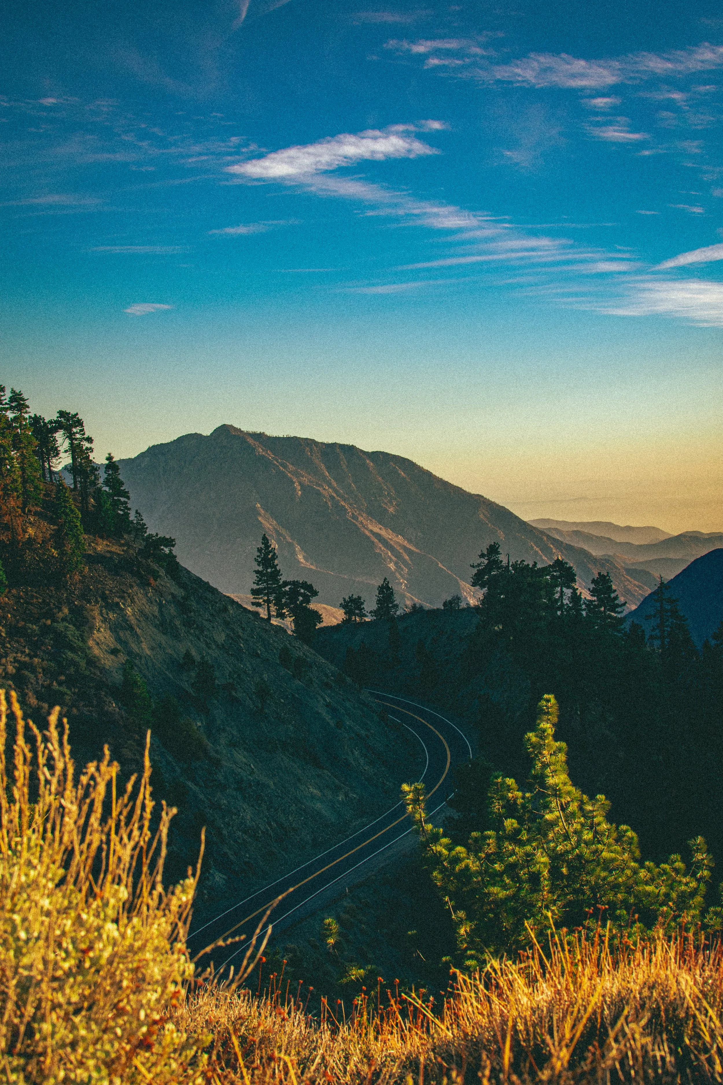 A scenic view of a mountain range during sunset with winding train tracks running through the forested hills.