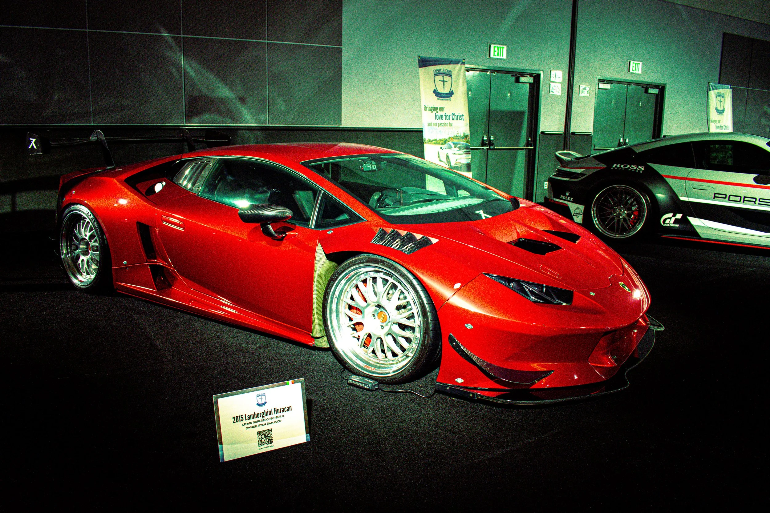 Red Lamborghini Huracan race car on display at a car exhibit, with a sign in front indicating it is a 2015 model.