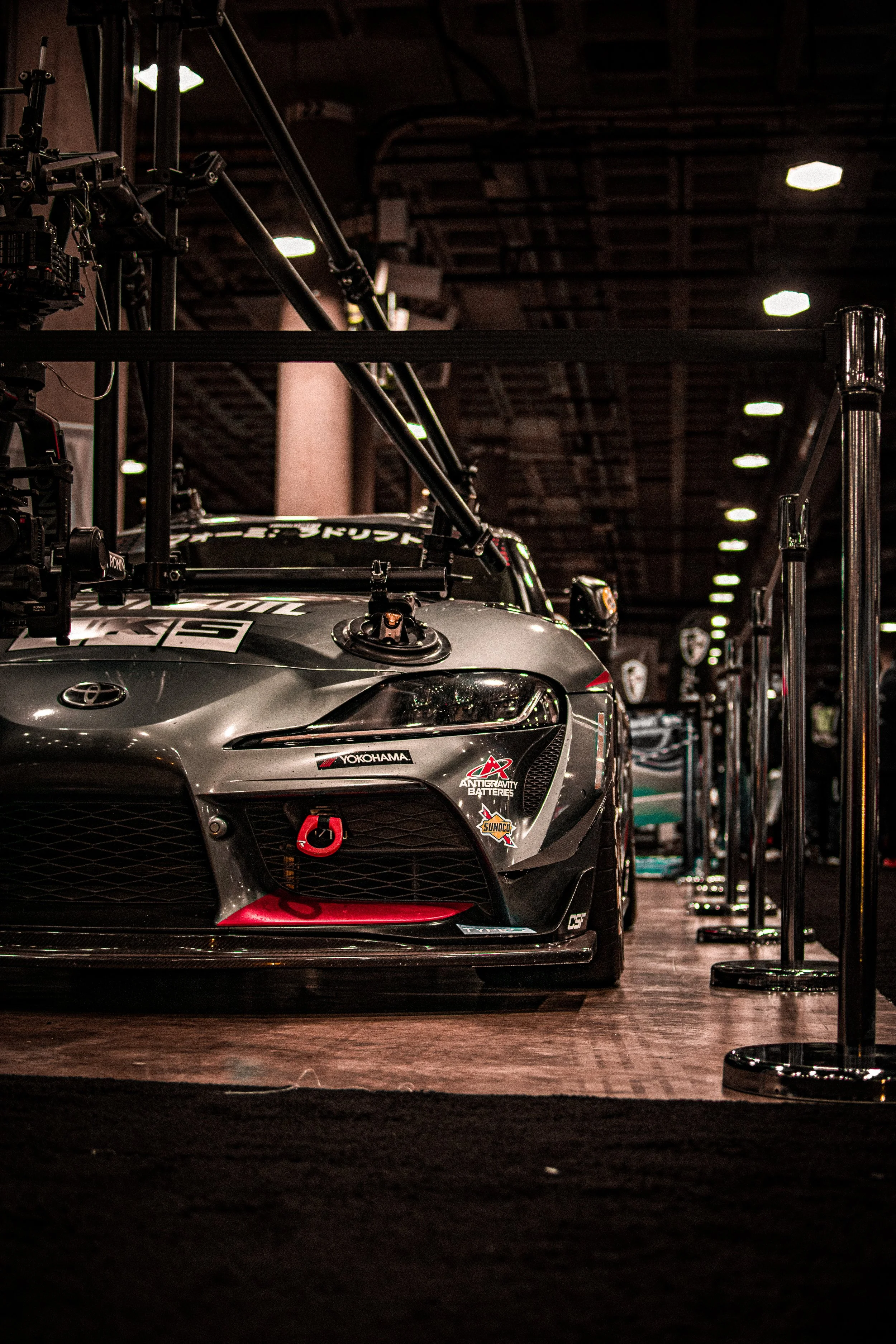 Close-up of a racing car in a garage, with visible sponsors and a red tow hook on the front.