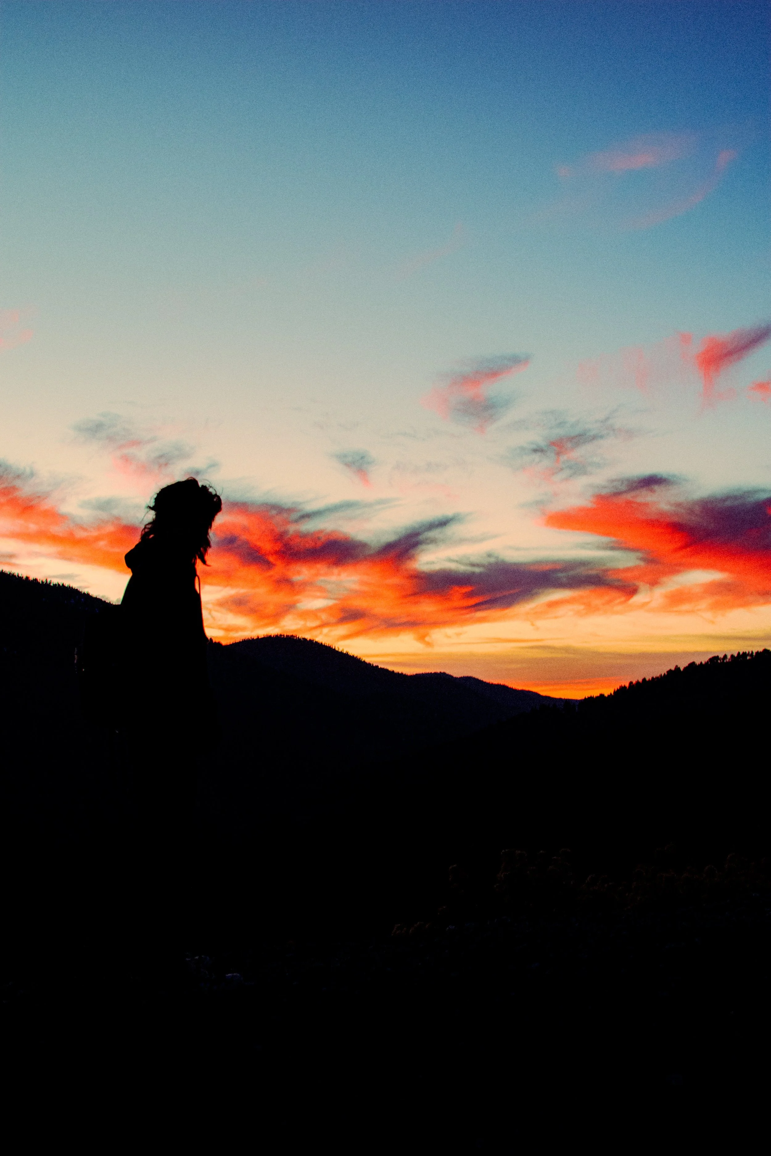 Silhouette of a person standing against a colorful sunset sky over hills.