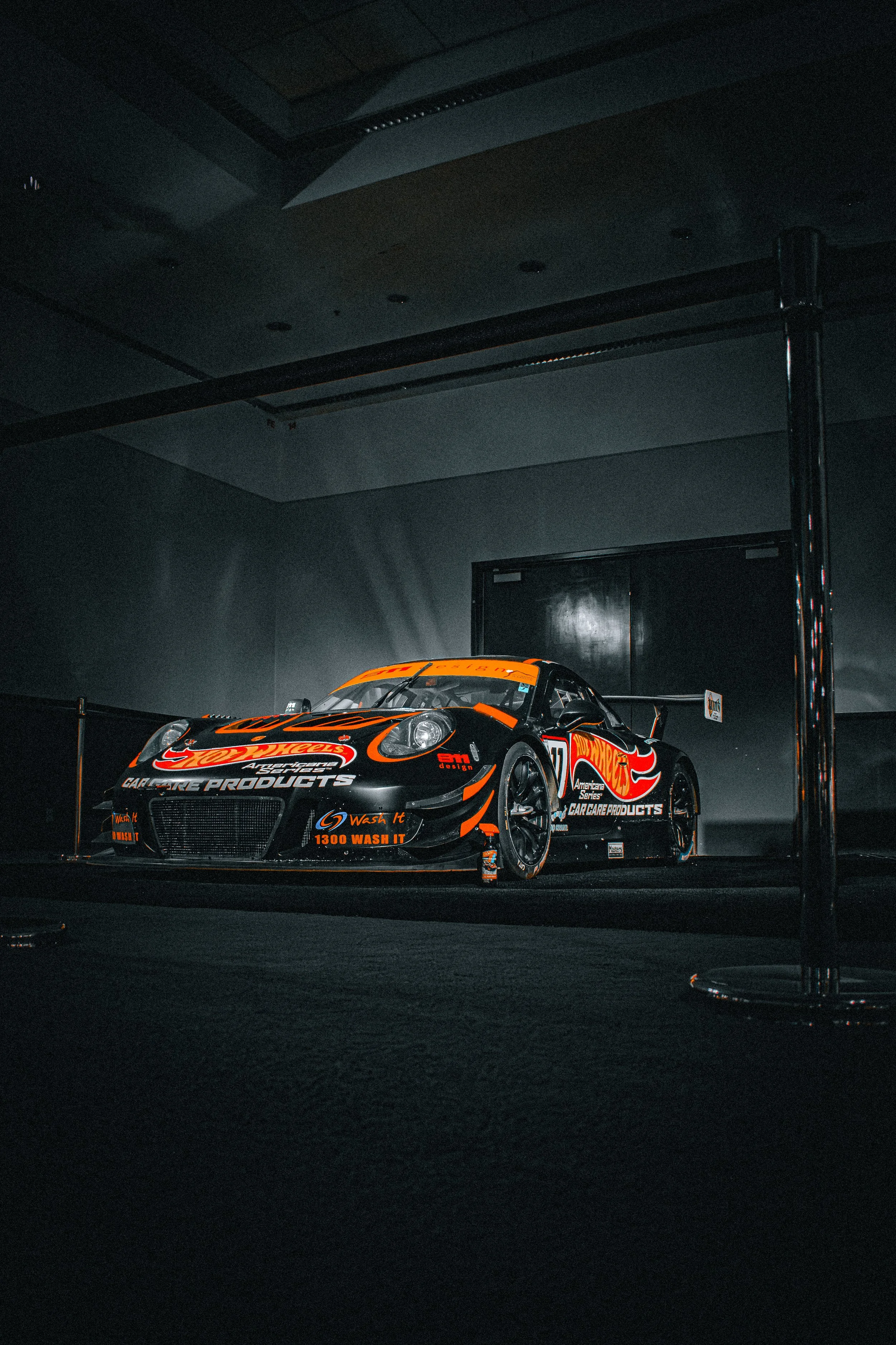 A black race car with orange and red flame graphics, displayed indoors with a velvet rope barrier in front.