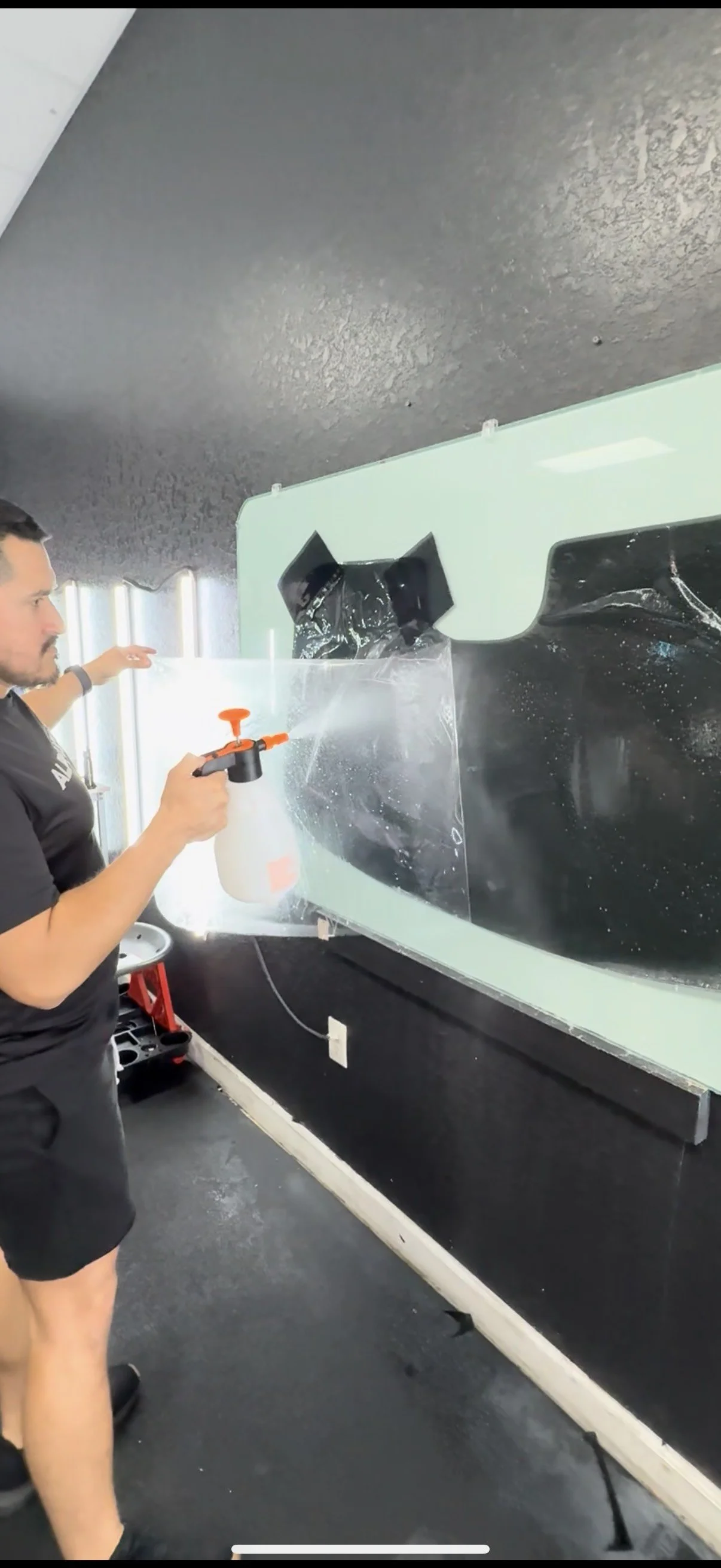 A man sprays cleaning solution onto a large glass surface using a spray bottle.