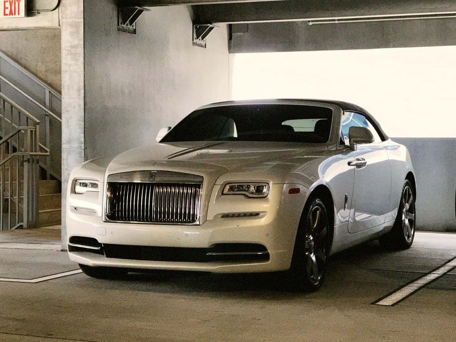 A white luxury convertible car parked in a dimly lit indoor parking garage.