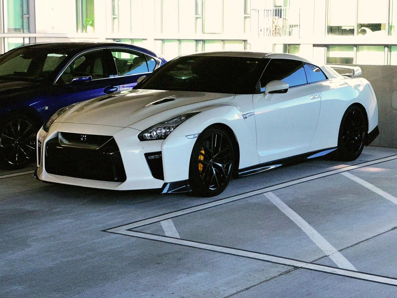 A white sports car with black wheels and tinted windows parked in an indoor parking garage.