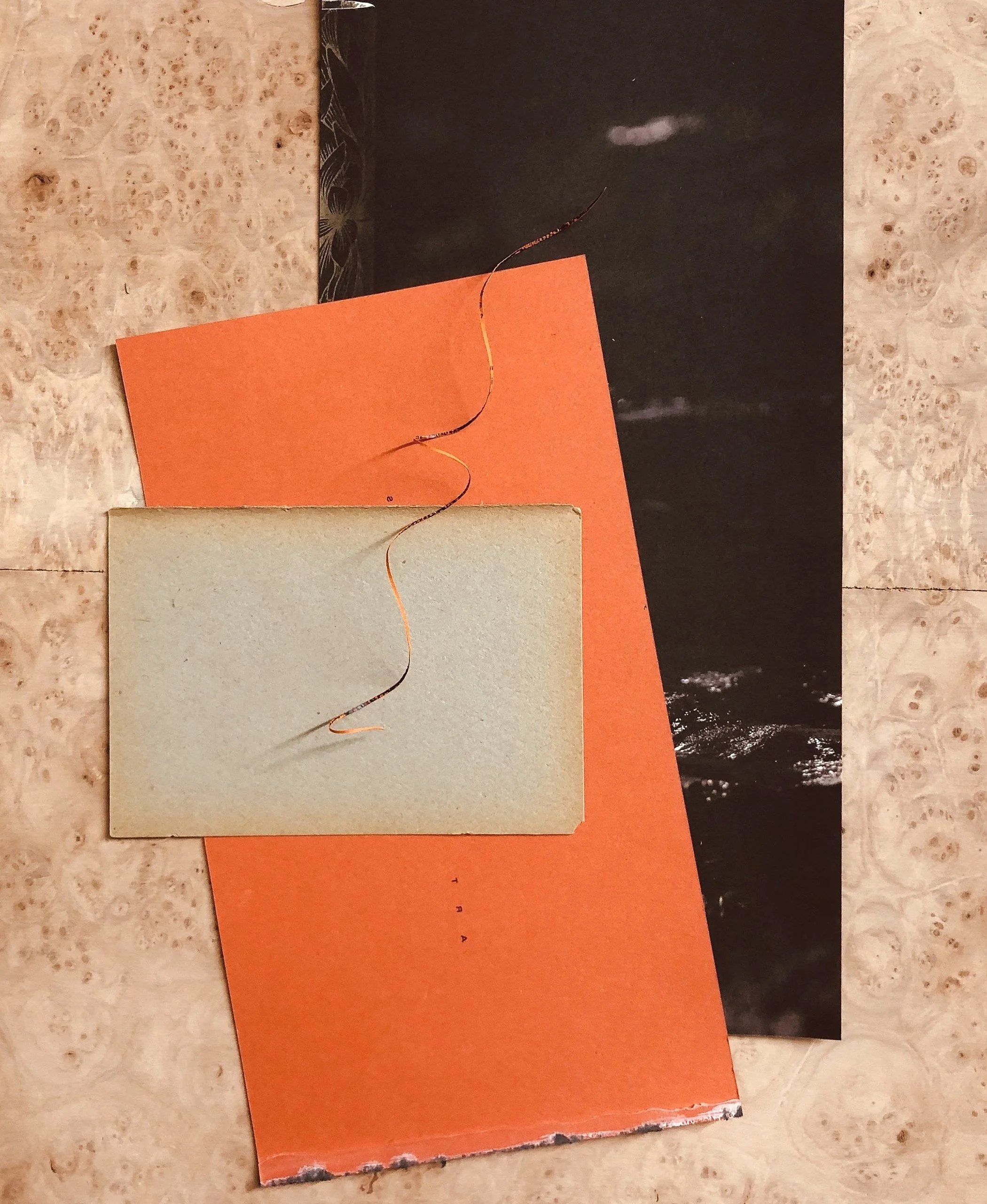 A spiral wire on top of a beige book, an orange piece of paper, and a black and white photo or print, all arranged on a textured light-colored surface.