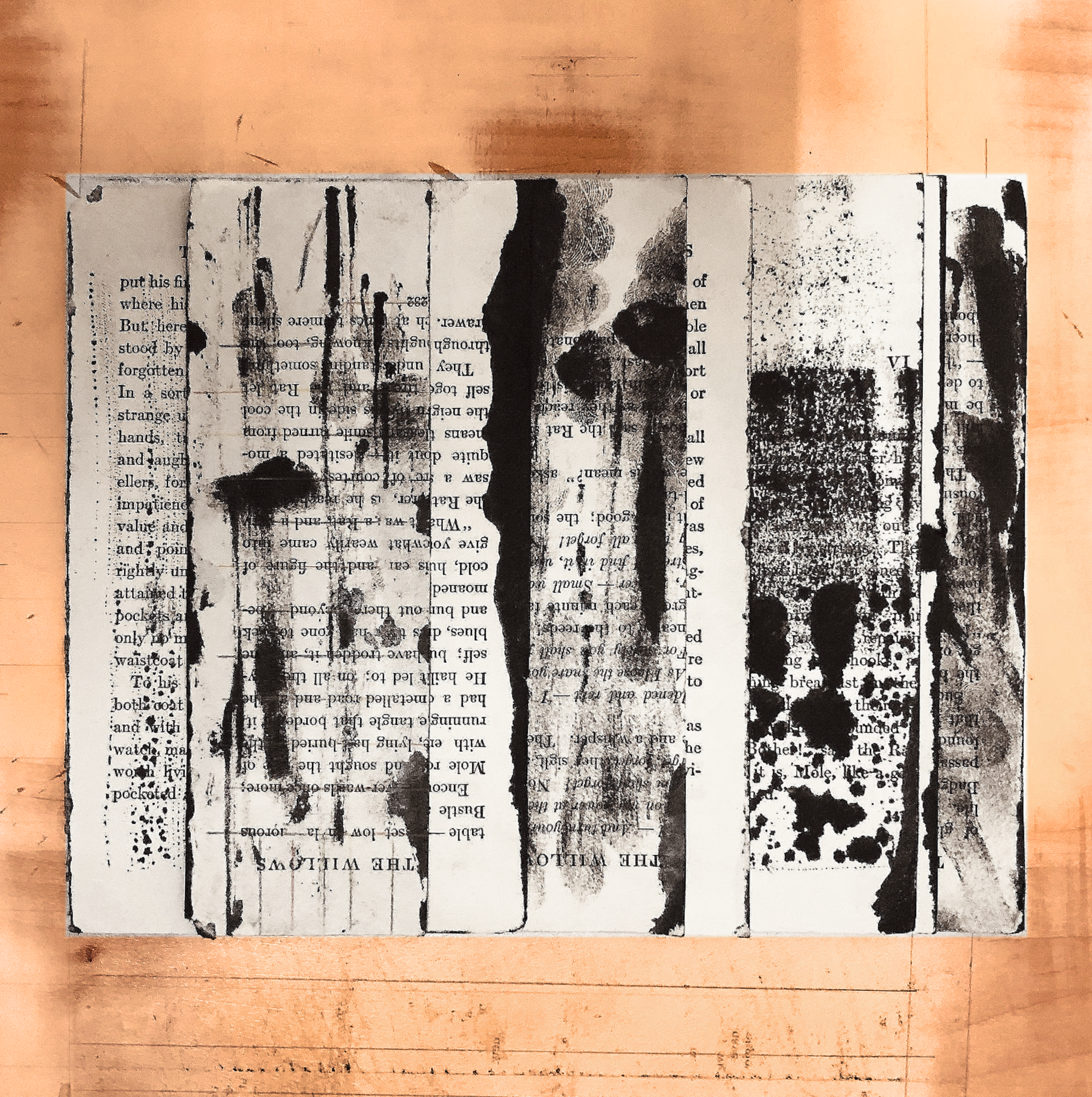 A sheet of paper with handwritten black ink splatters and streaks, placed on a wooden surface with faint pencil markings.